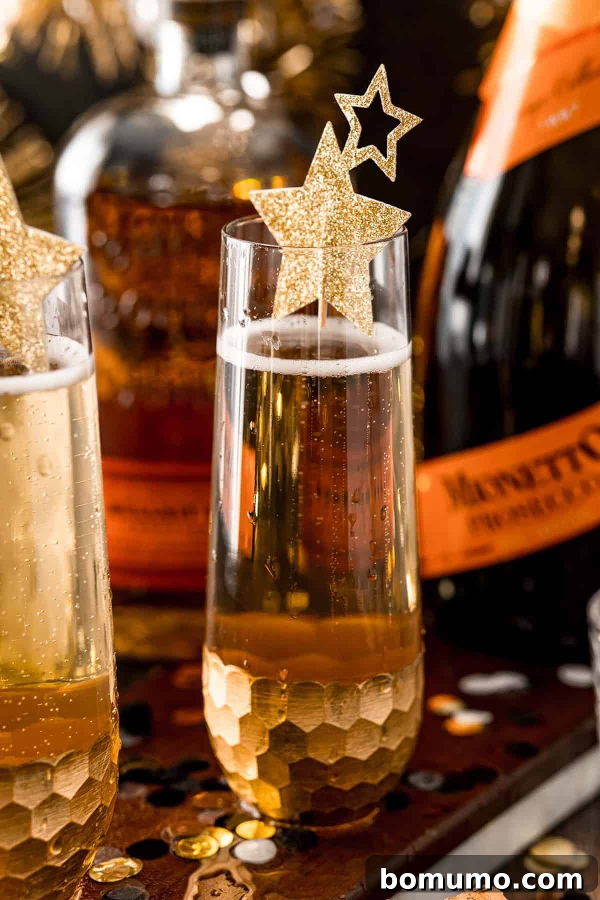 A festive vanilla bourbon fizz cocktail in a stemless champagne glass, garnished with delicate gold stars, sparkling beautifully.