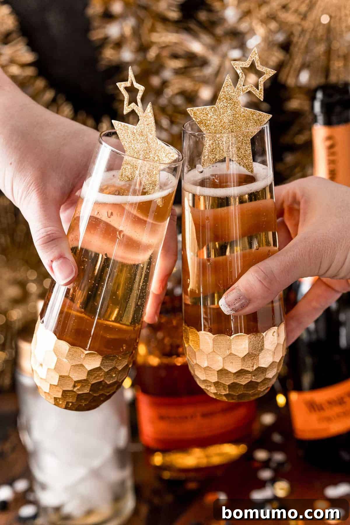 Two hands gently holding elegant stemless champagne flutes, each filled with the inviting light brown hue of a vanilla bourbon fizz cocktail.