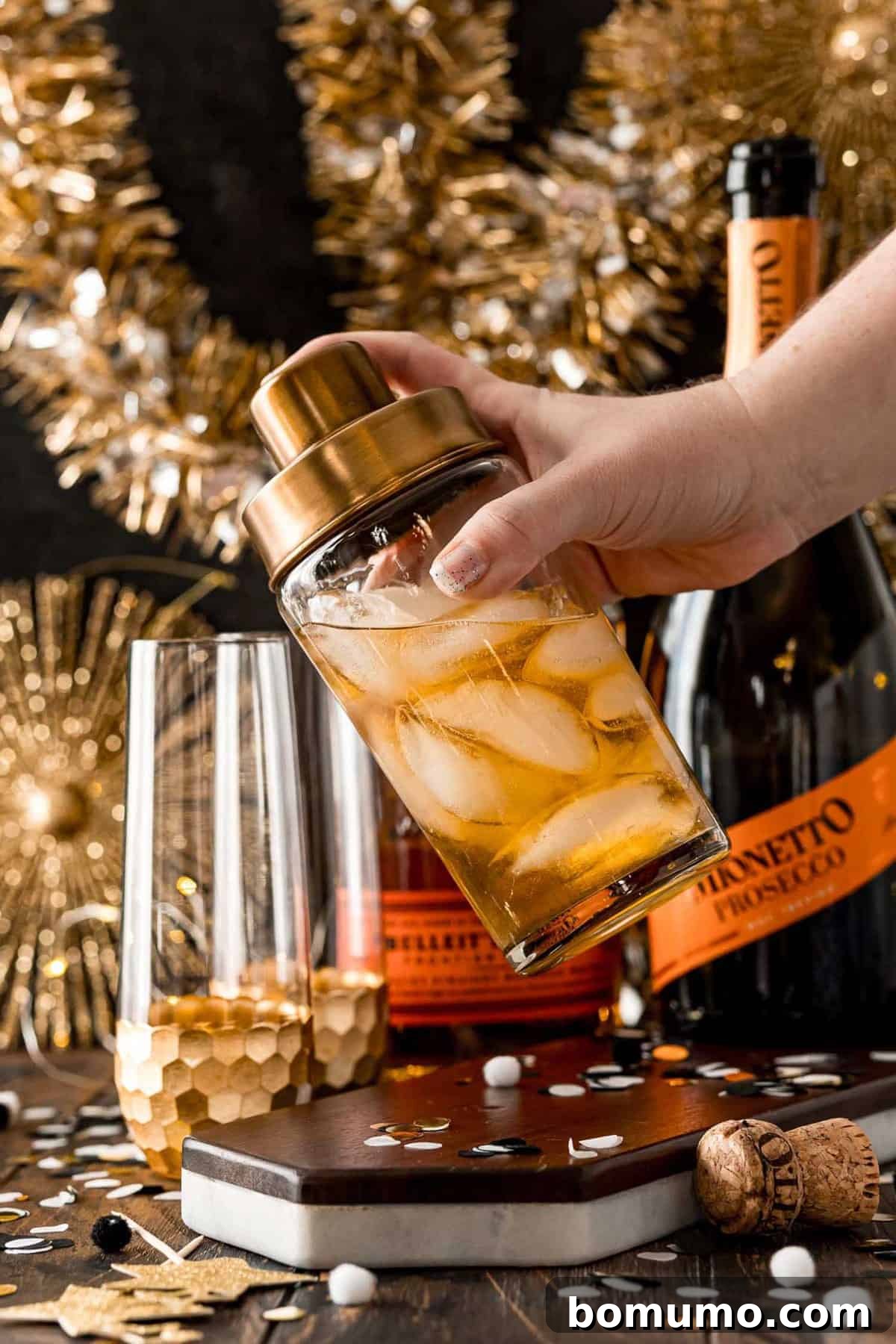 A sleek cocktail shaker, filled with a rich, light brown liquid and shimmering ice cubes, ready to be transformed into a refreshing vanilla bourbon fizz.