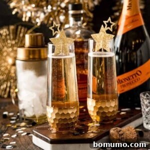 Two stemless champagne glasses featuring the Vanilla Bourbon Fizz, with a cocktail shaker, ice, bourbon bottle, and prosecco bottle in the background. Drinks are garnished with delicate gold stars.
