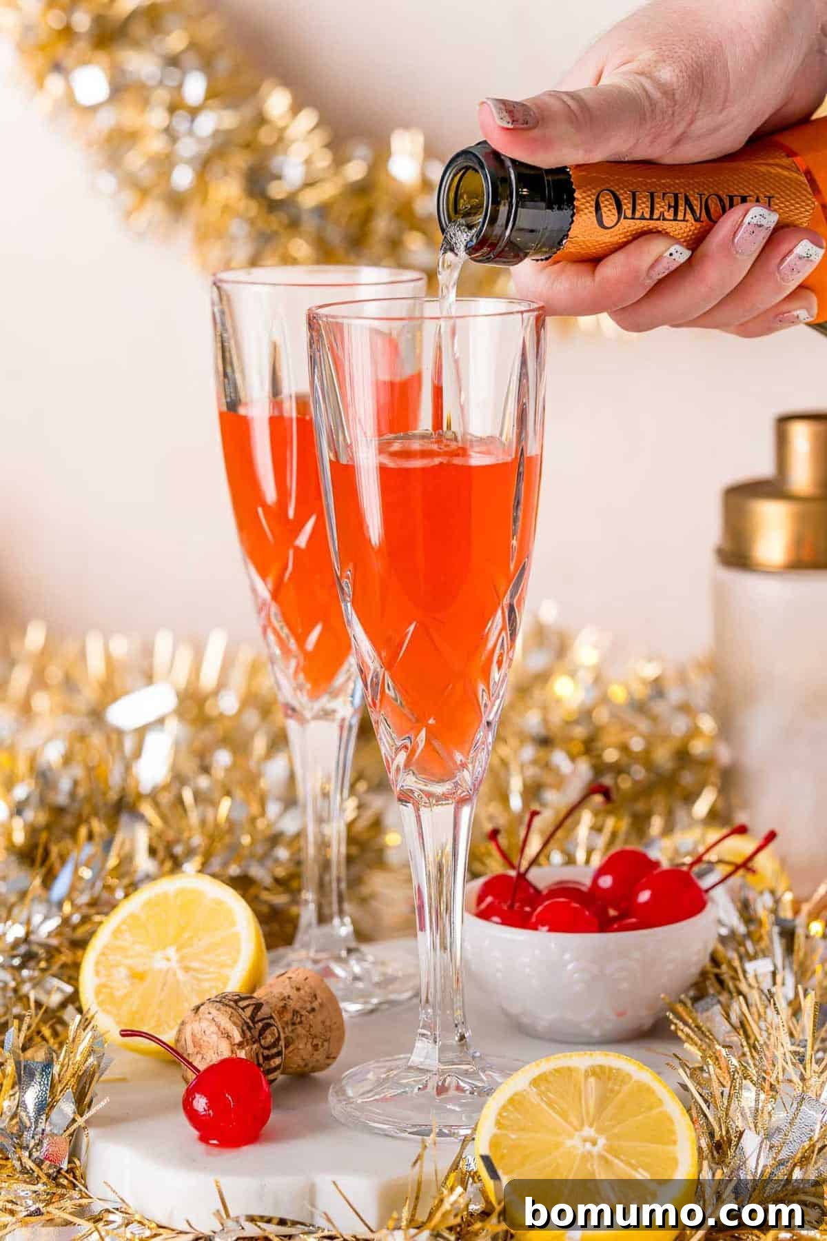Champagne being poured into a champagne glass already partially full of light red liquid.