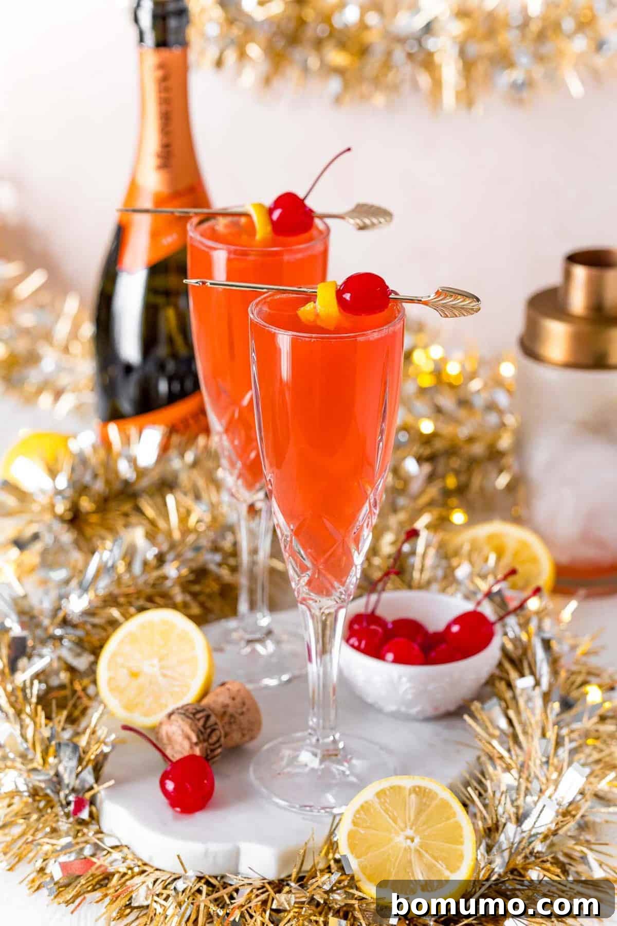 Festive scene with two champagne glasses, lemons, cherries, and gold garland.
