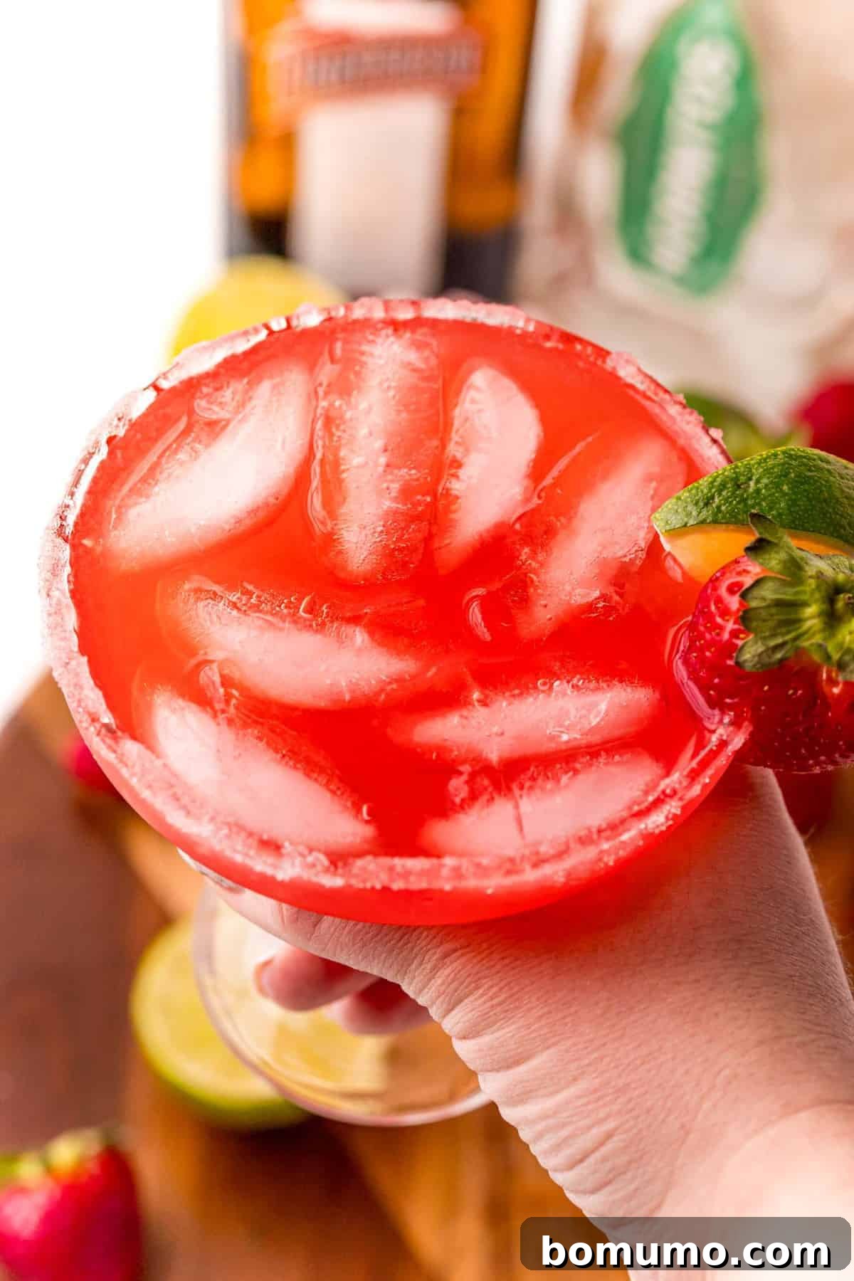 Glass of punch garnished with strawberry being held in a hand.