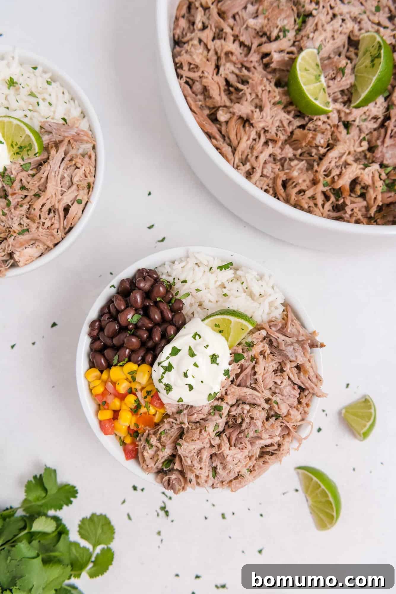 Overhead view of Slow Cooker Cuban Pork served in a vibrant bowl with rice, black beans, and corn, positioned next to a larger serving dish of the shredded pork.