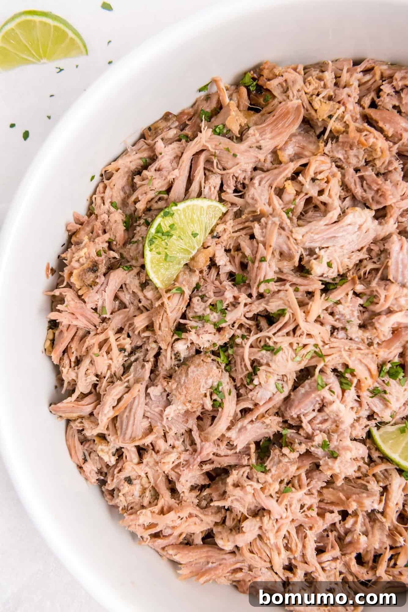 Large white platter of Slow Cooker Cuban Pork garnished with fresh lime wedges, beautifully presented and ready to serve at a gathering.