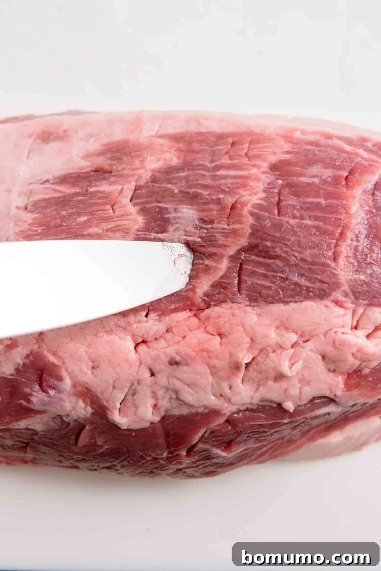 Close-up of a boneless pork shoulder being carefully cut with a knife, demonstrating how to pierce the meat for optimal marinade absorption.