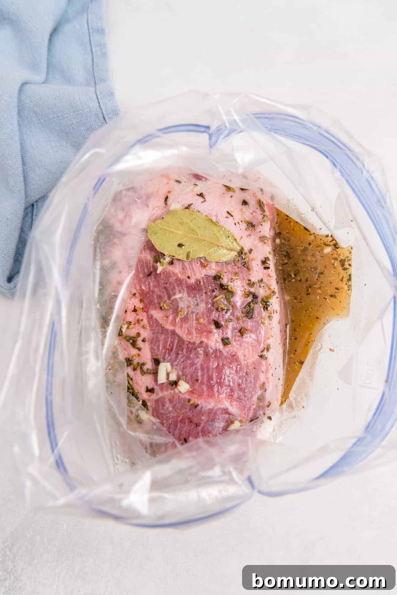 Pork shoulder soaking in a vibrant citrus-garlic marinade inside a sturdy zip-top bag, with bay leaves visible, ready for overnight refrigeration.