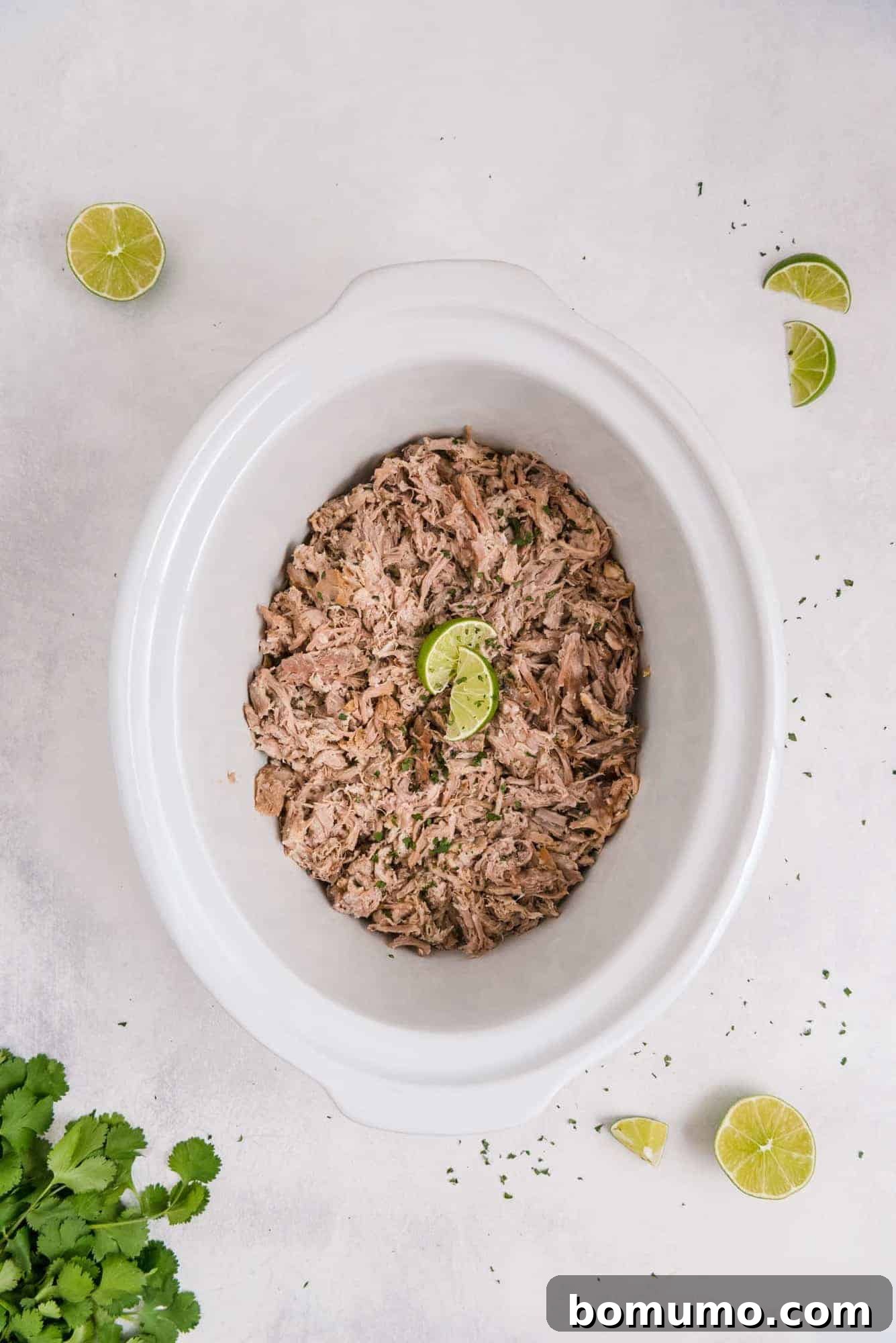Perfectly pulled and shredded Cuban pork resting in a white crock pot, surrounded by its flavorful juices, ready to be served.