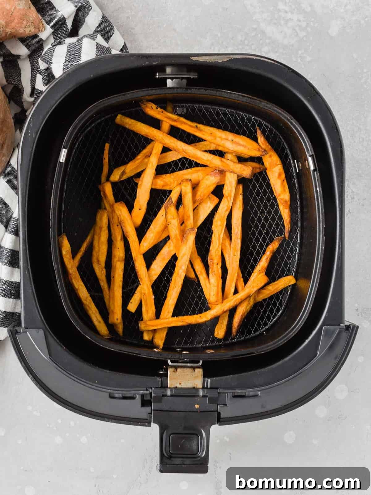 Close-up overhead view of perfectly cooked, golden-brown sweet potato fries resting in the basket of an air fryer, ready to be served.