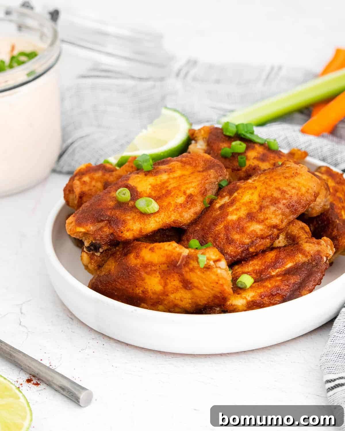 Glazed chili lime chicken wings on a white plate, garnished with fresh green onions and vibrant lime wedges.