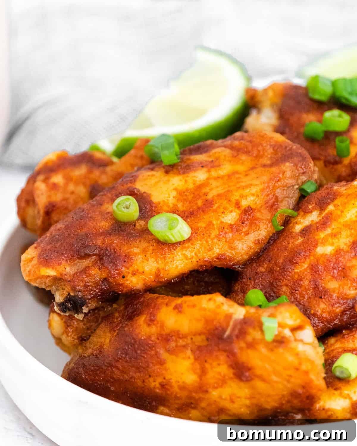 Close-up of perfectly glazed chili lime chicken wings on a white plate, beautifully garnished with chopped green onions.