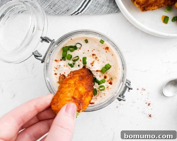 A chili lime chicken wing being enthusiastically dipped into the creamy sour cream sauce.