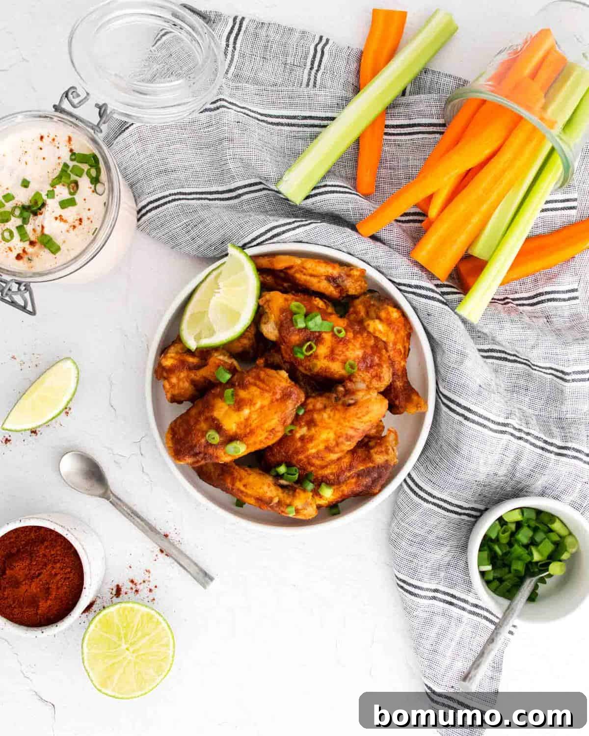 Overhead view of perfectly glazed chili lime chicken wings arranged with fresh carrot and celery sticks, and a small bowl of creamy dipping sauce.