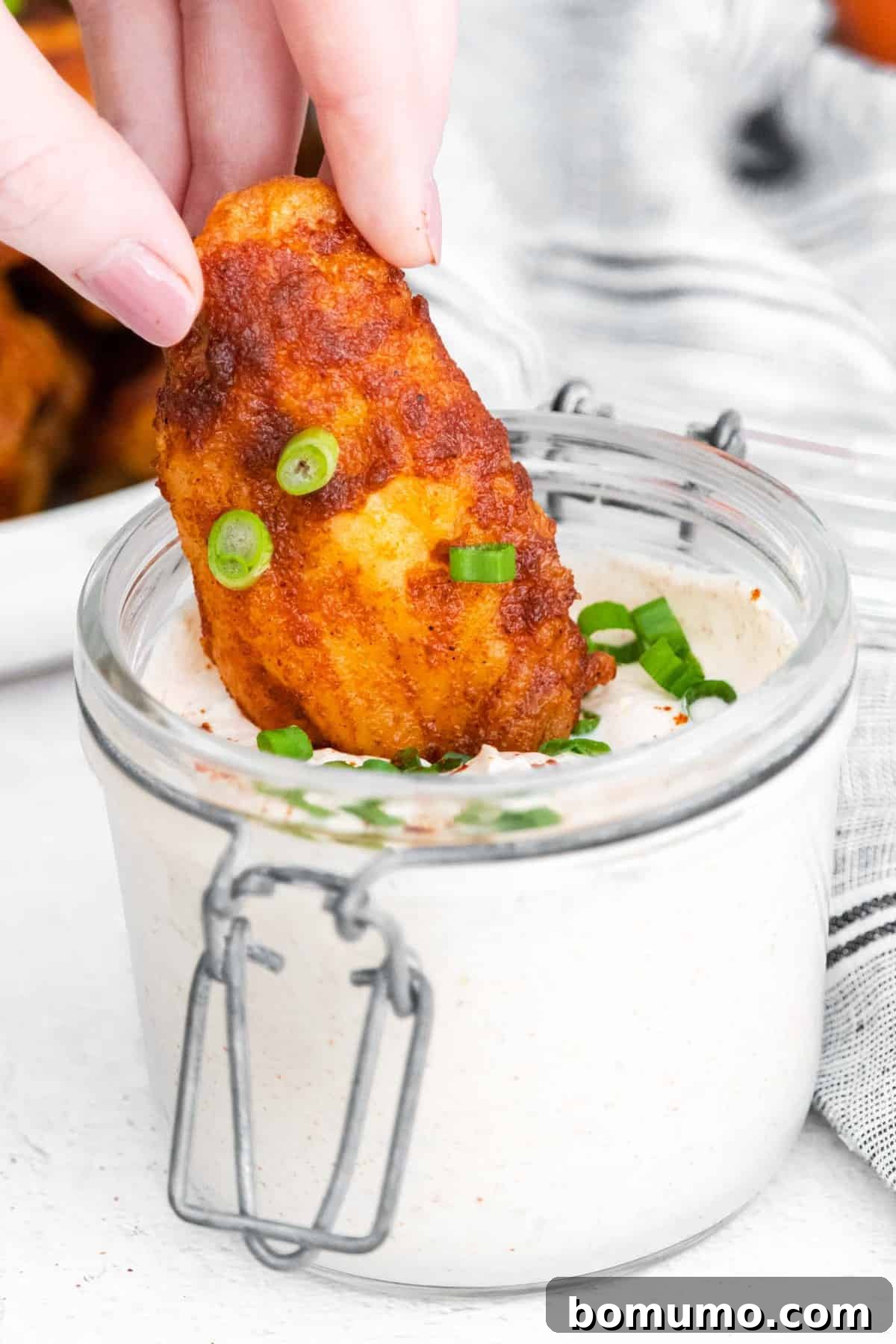 A close-up shot of a perfectly glazed chili lime chicken wing being dipped into a luscious sour cream sauce.