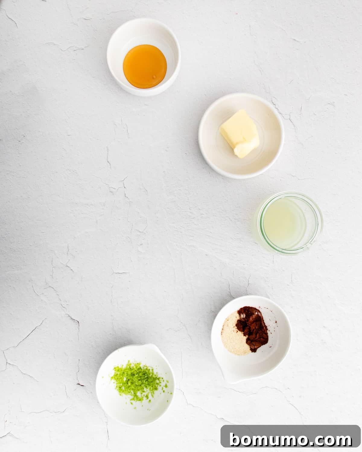 Small white bowls filled with the ingredients for the chili lime glaze: butter, honey, lime juice, lime zest, chili powder, garlic powder, and salt.