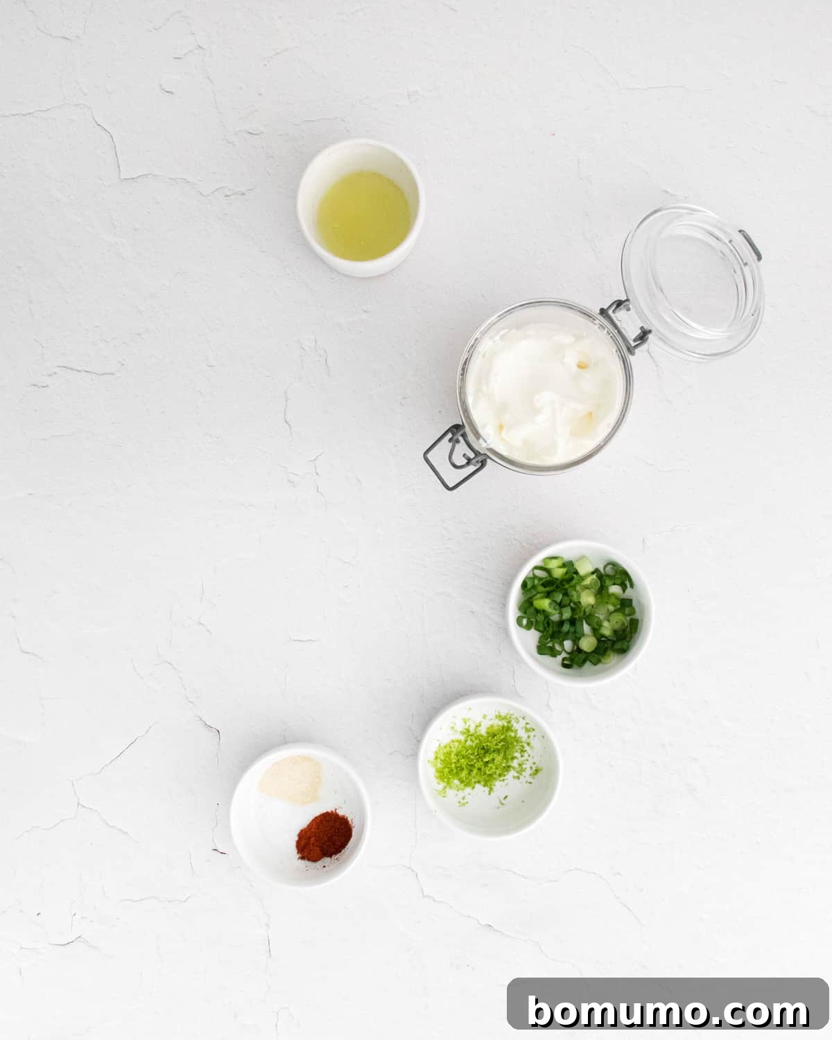 A collection of small bowls showcasing the fresh ingredients for the sour cream dip: sour cream, lime juice, sliced green onions, garlic powder, paprika, and lime zest.