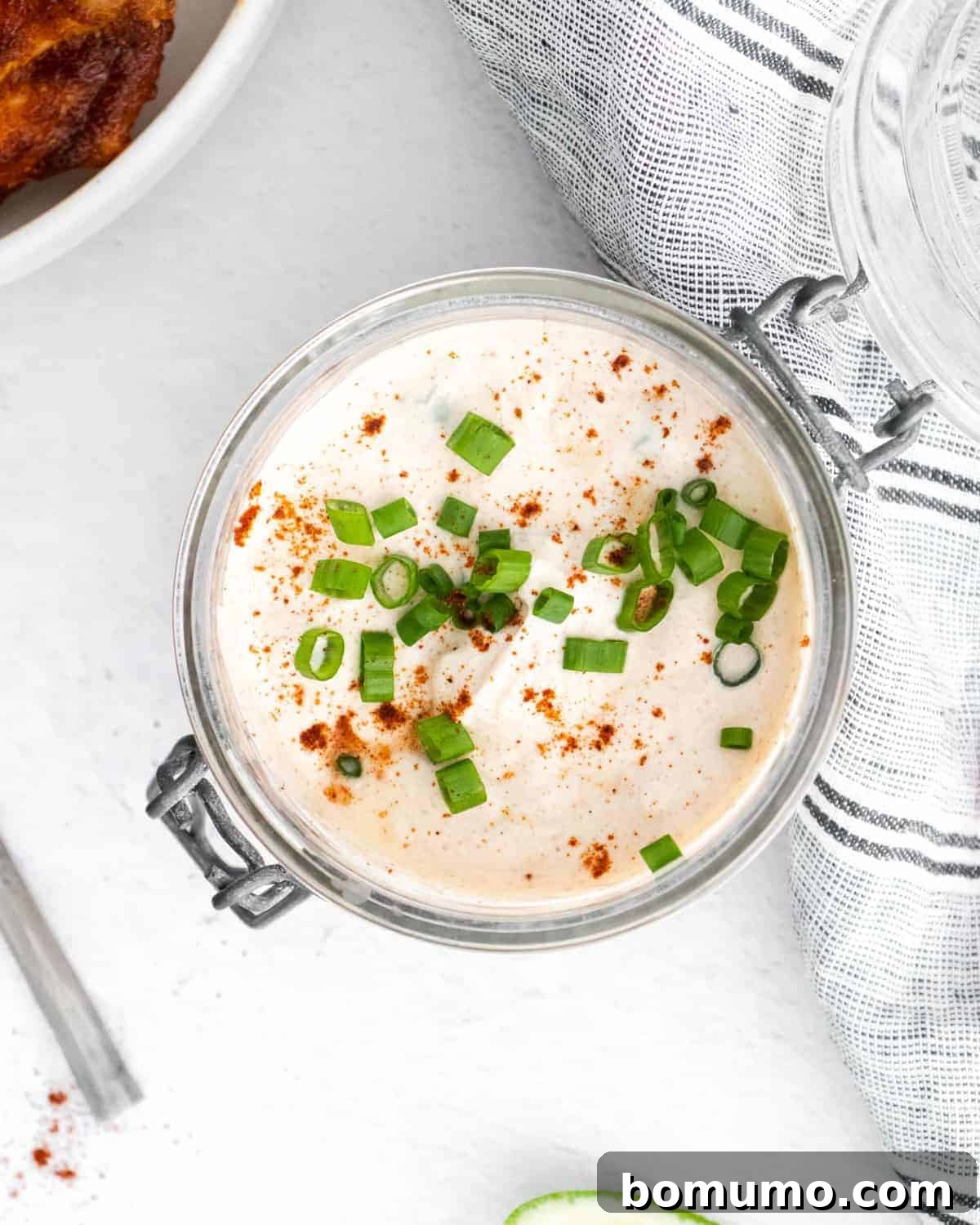 A bowl of creamy sour cream dip, richly garnished with chili powder, fresh green onions, and vibrant lime zest.