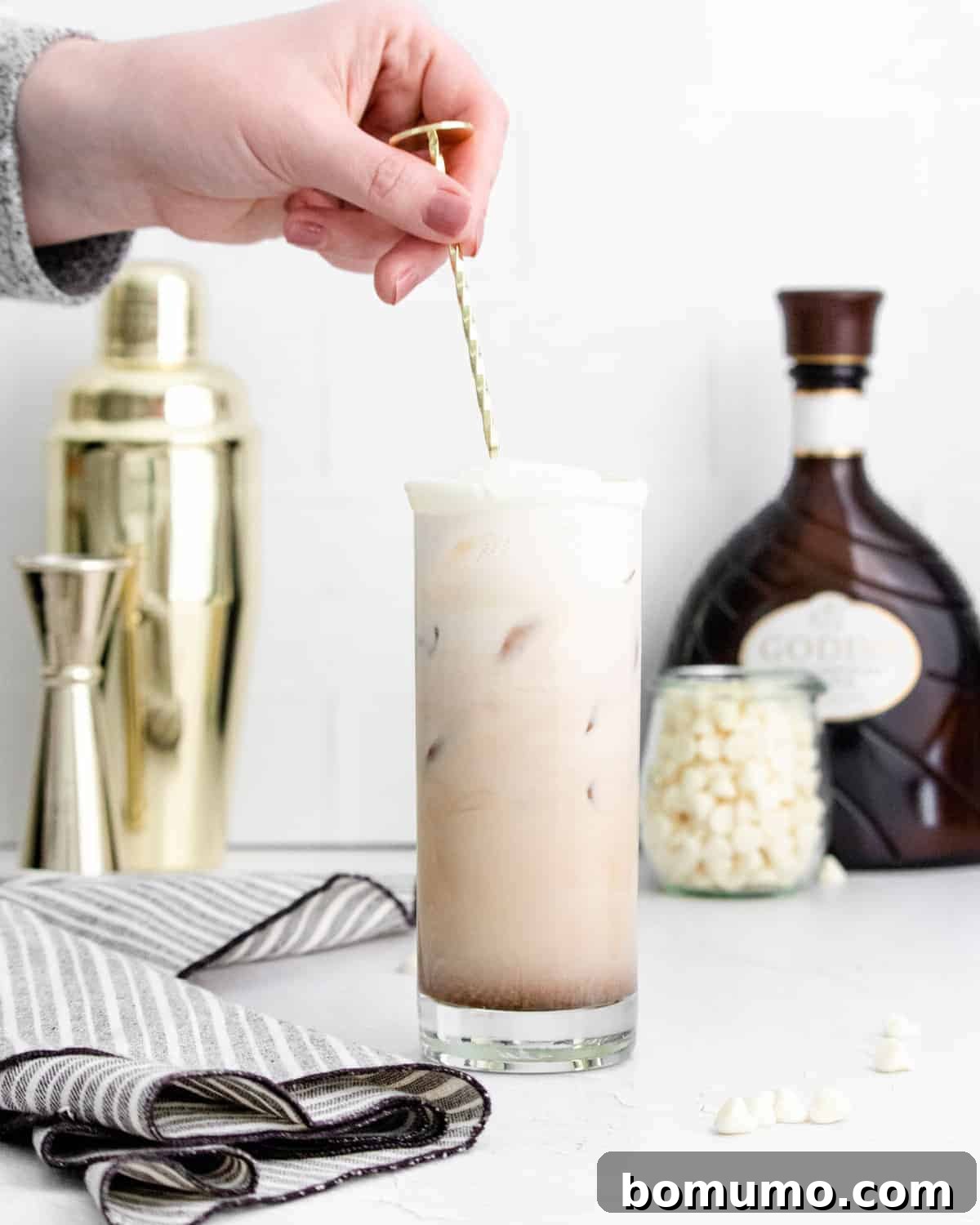 A tall, elegant White Russian cocktail, perfectly iced and being stirred gently in a clear glass, showcasing its creamy texture.