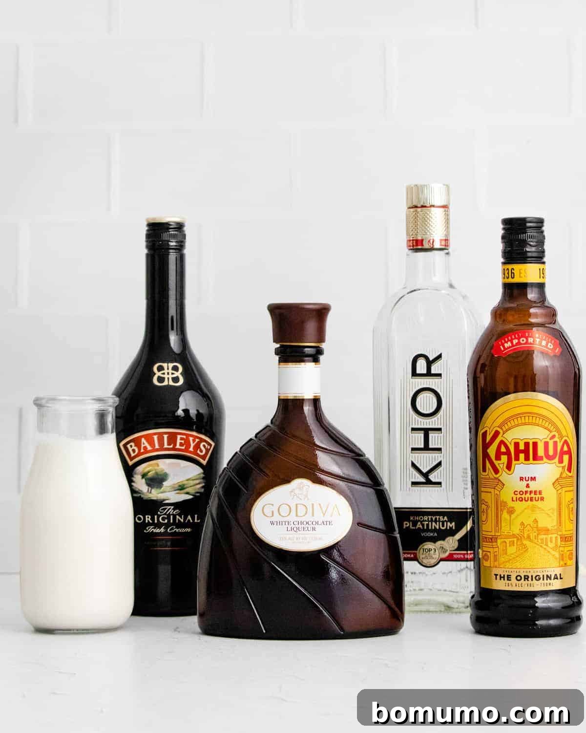 A perfectly arranged lineup of the core ingredients for a White Chocolate White Russian: half-and-half, Bailey's Irish Cream, white chocolate liqueur, vodka, and Kahlúa.
