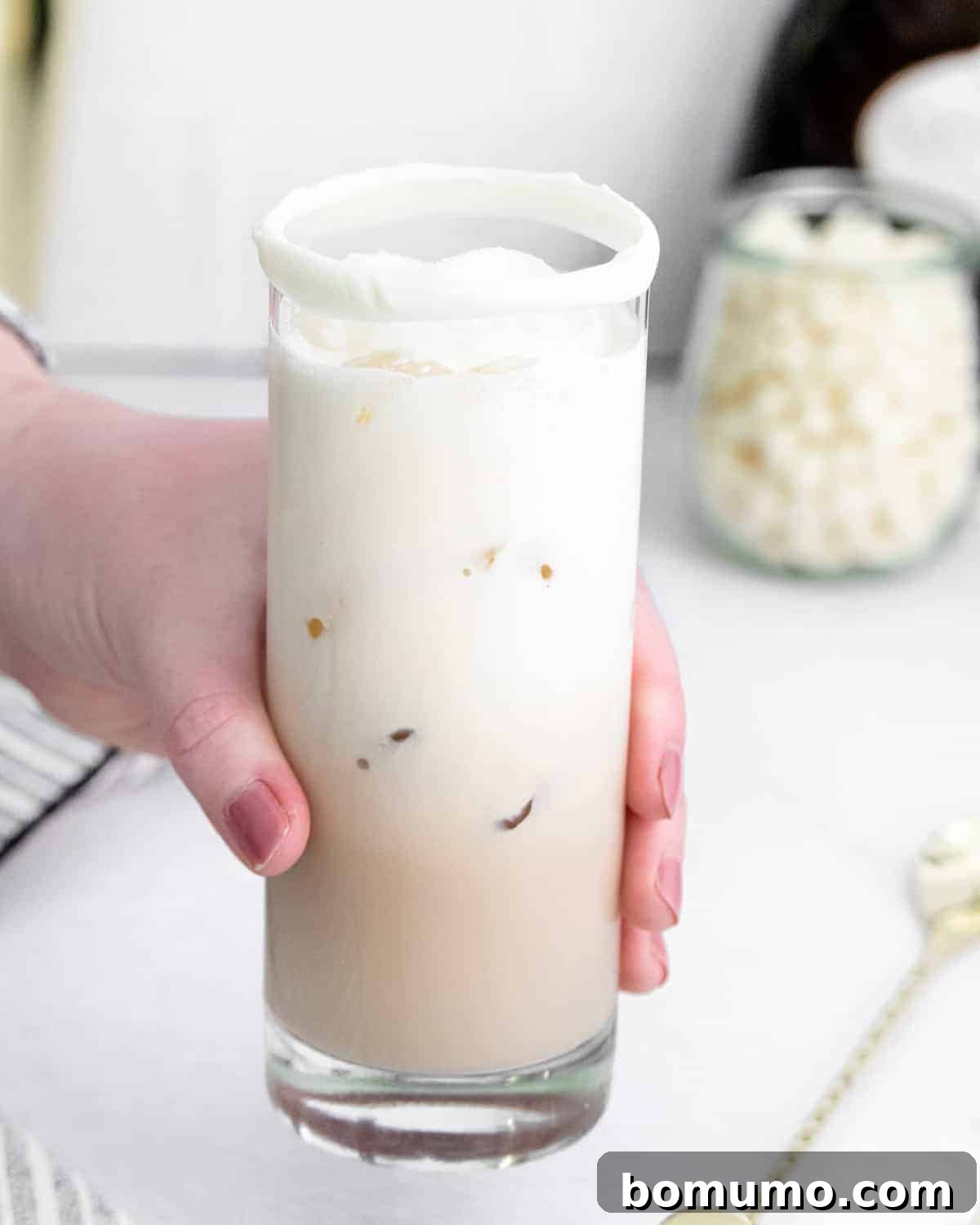 A hand gracefully holding a White Chocolate White Russian cocktail, showcasing its inviting layers and elegant presentation.