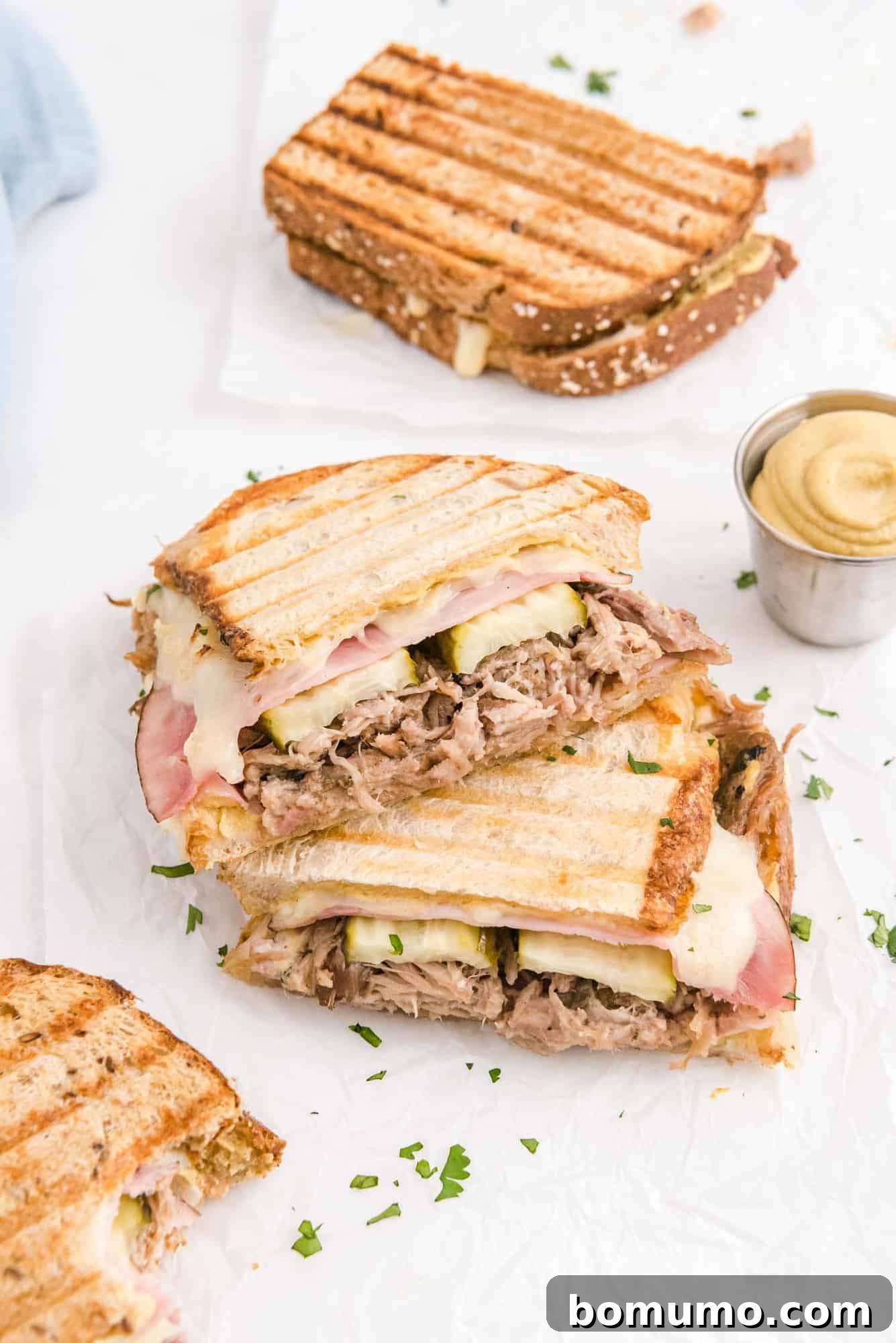 Ultimate Cuban Sandwich 2 Two halves of a perfectly grilled Cuban sandwich, stacked enticingly with layers of pork, ham, cheese, and pickles visible.