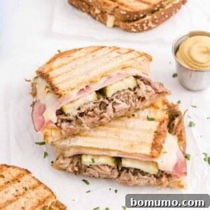 Cuban panini sliced in half, halves stacked on top of each other, on a white surface.