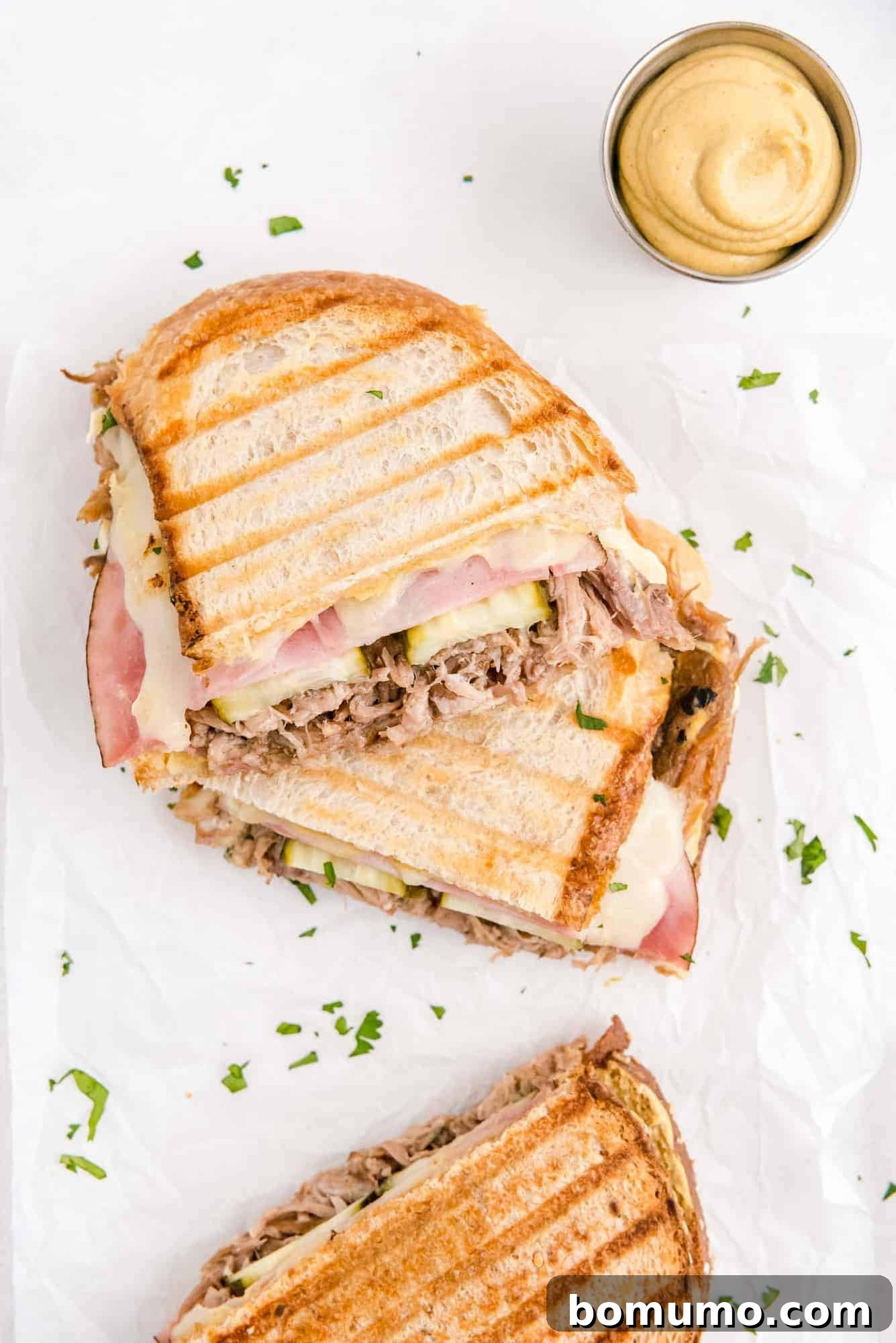 Ultimate Cuban Sandwich 3 An overhead view of a freshly cut Cuban sandwich, revealing its delicious layers, accompanied by a small dish of mustard.