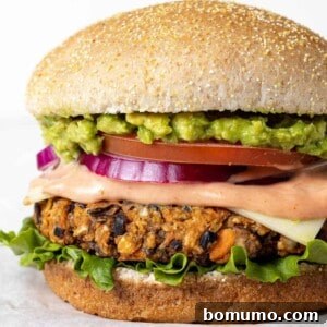 A delicious homemade black bean burger on a whole wheat bun, generously topped with fresh guacamole, crisp red onion, ripe tomato, and green lettuce for a satisfying and healthy meal.