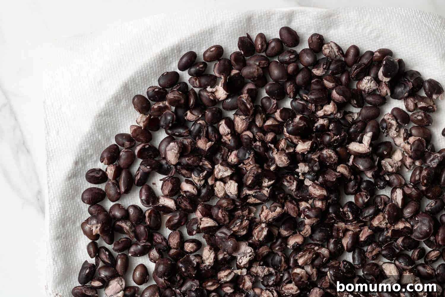 Savory Black Bean Bliss 5 Drained and rinsed black beans spread evenly on a paper towel-lined white plate, ready for microwave drying to achieve a firmer texture.