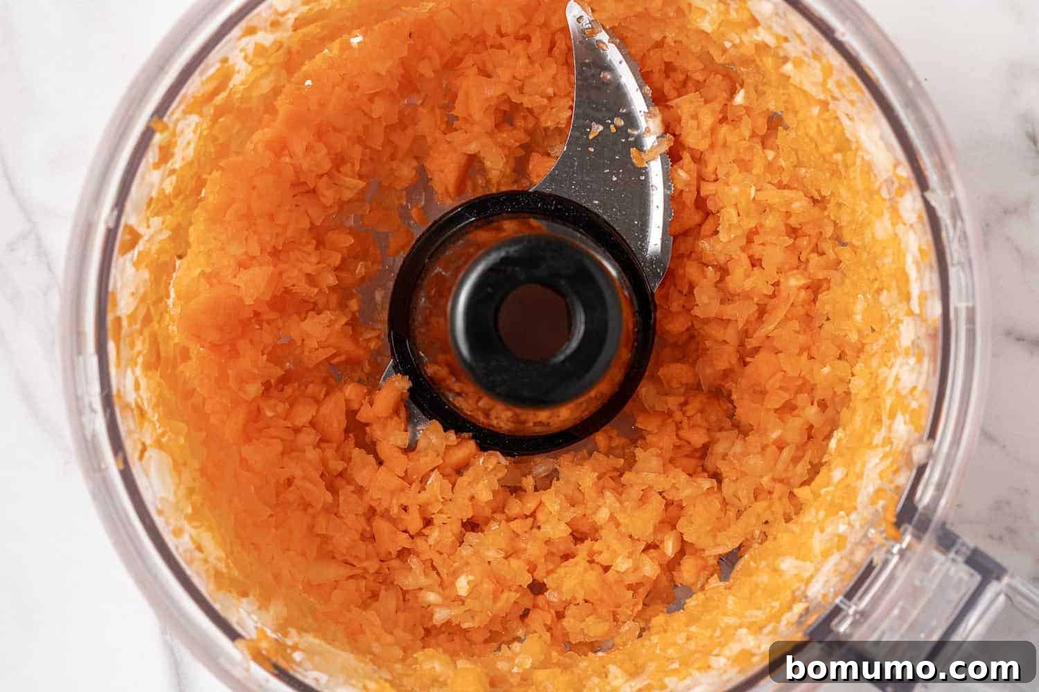Savory Black Bean Bliss 7 Perfectly chopped carrots and onions, finely minced and ready for the black bean burger mix, displayed in a food processor bowl.
