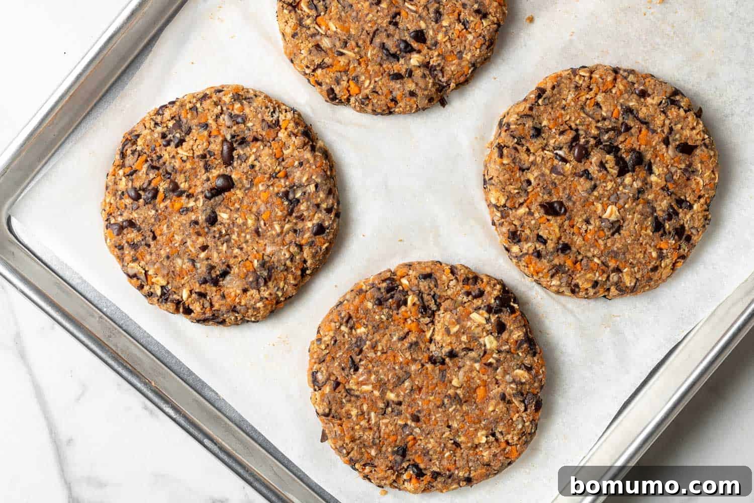 Savory Black Bean Bliss 10 Four perfectly formed black bean burgers neatly arranged on a parchment paper-lined baking sheet, ready for baking or freezing.
