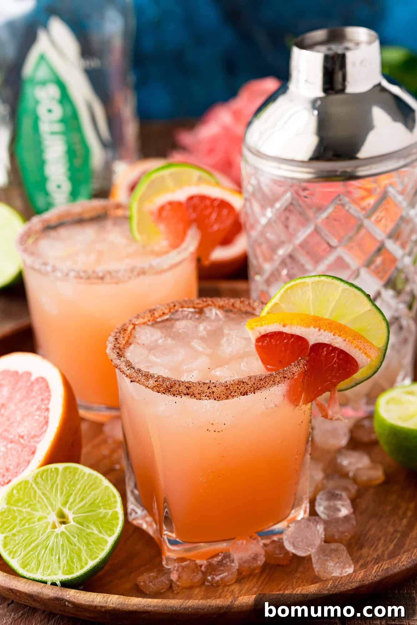 Two light pink cocktails on ice, garnished with grapefruit and lime.