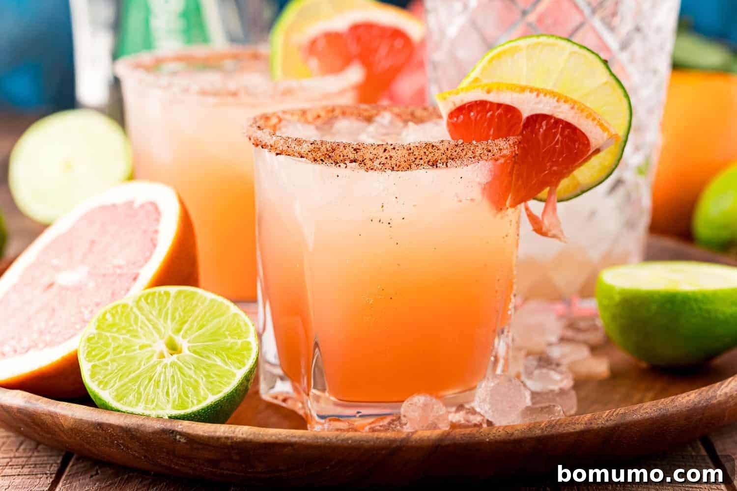 Light orange-pink cocktails on a wooden tray with ice, limes, grapefruits.