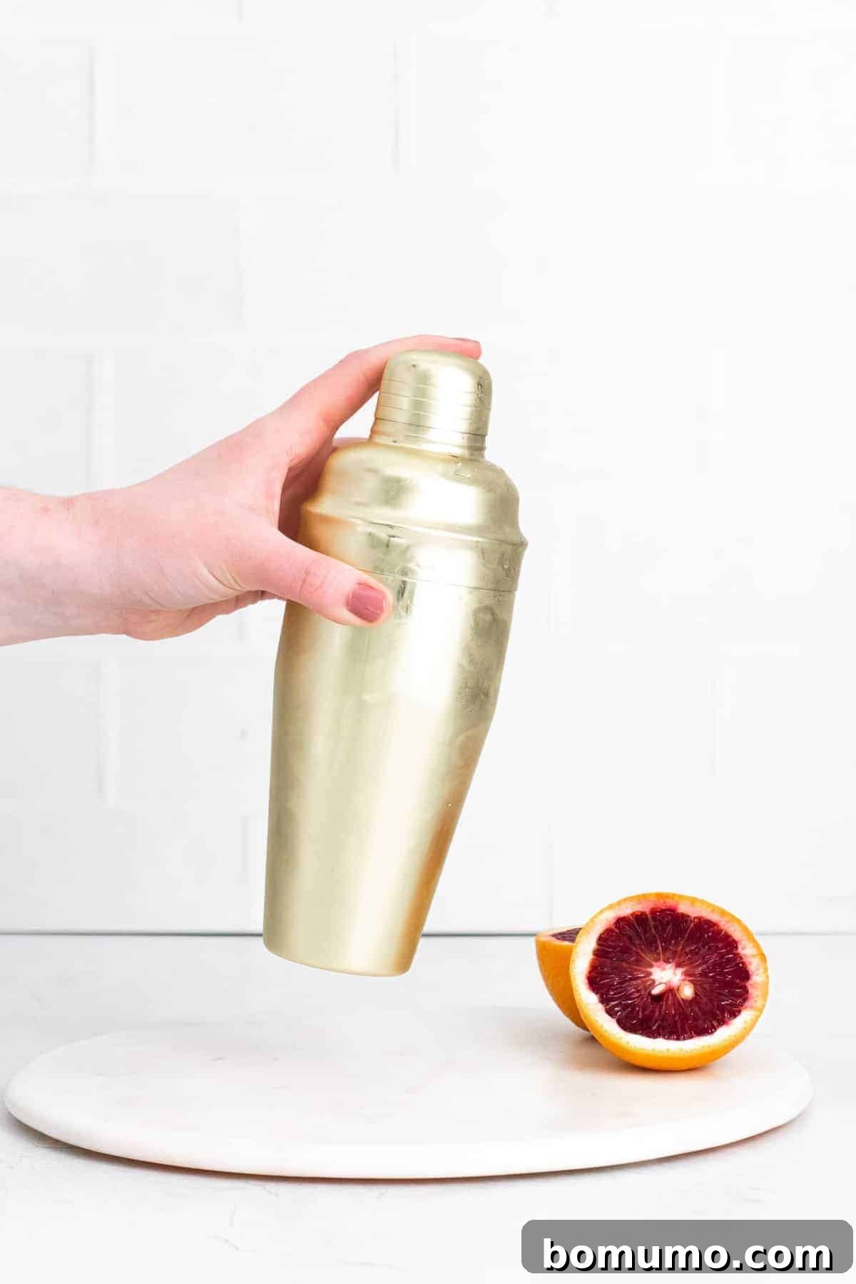 Gold cocktail shaker being shaken. Mixing a Blood Orange Gin Fizz.