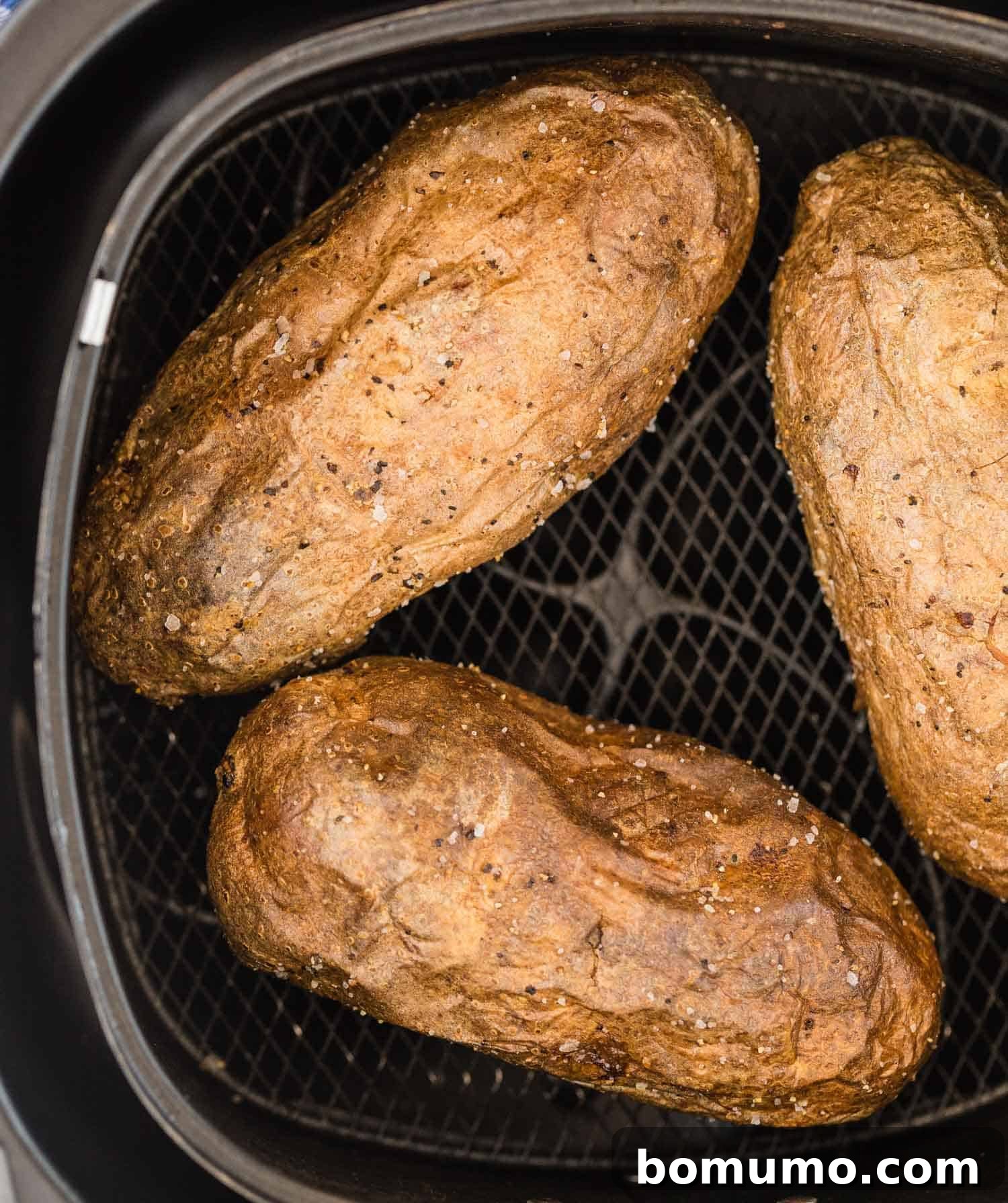 Close up view of perfectly golden-brown baked potatoes resting in an air fryer basket, ready to be served.
