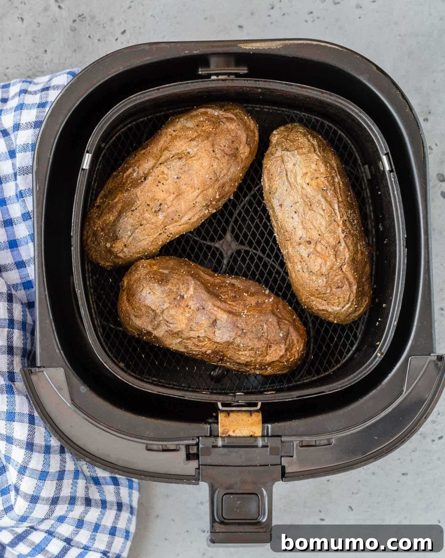 Overhead view of several golden, perfectly baked potatoes nestled in the basket of an air fryer.