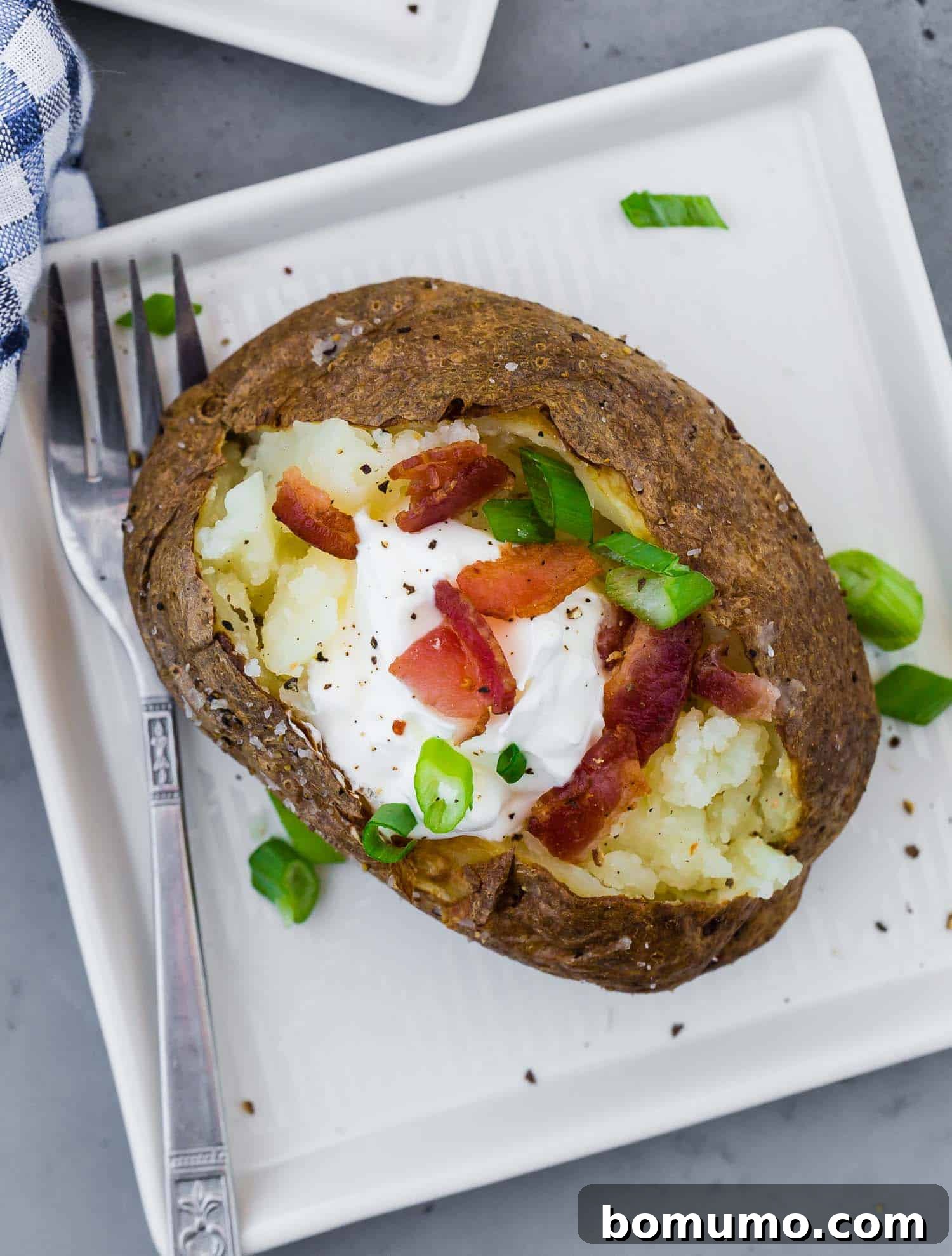 Overhead view of a perfectly baked potato generously topped with creamy sour cream, vibrant green onions, and savory crispy bacon.