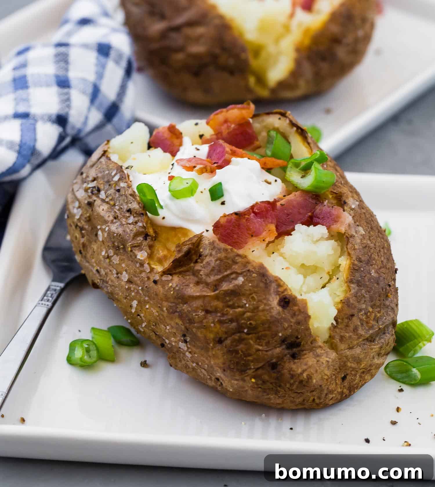 A beautifully prepared baked potato, brimming with delicious toppings, served on a pristine square white plate.