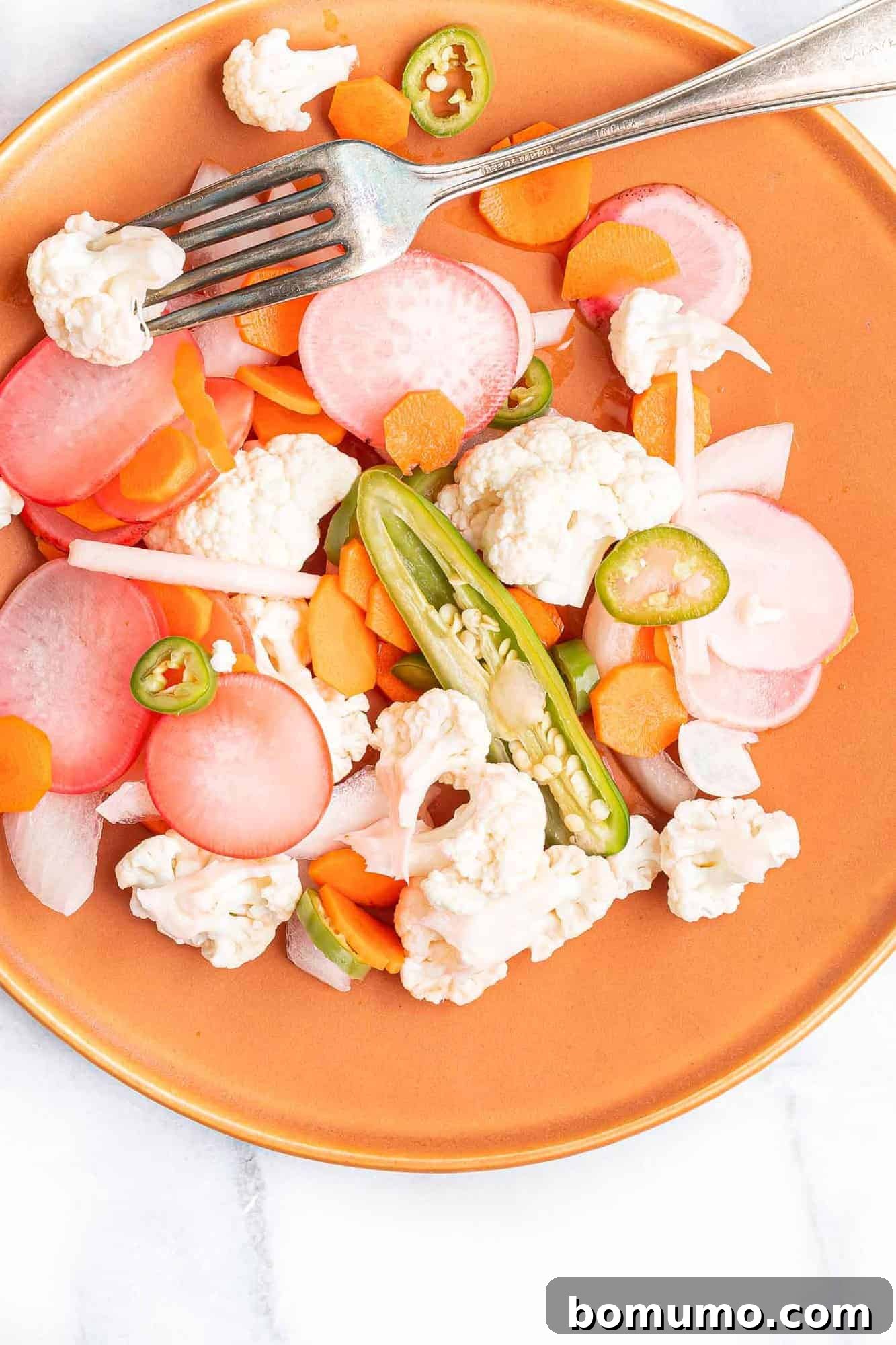 Pickled vegetables on a reddish orange plate, ready to be served.