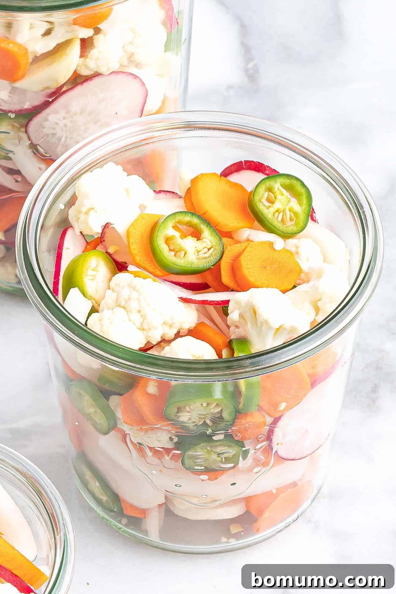 Assorted cut vegetables packed tightly into a clear glass jar.