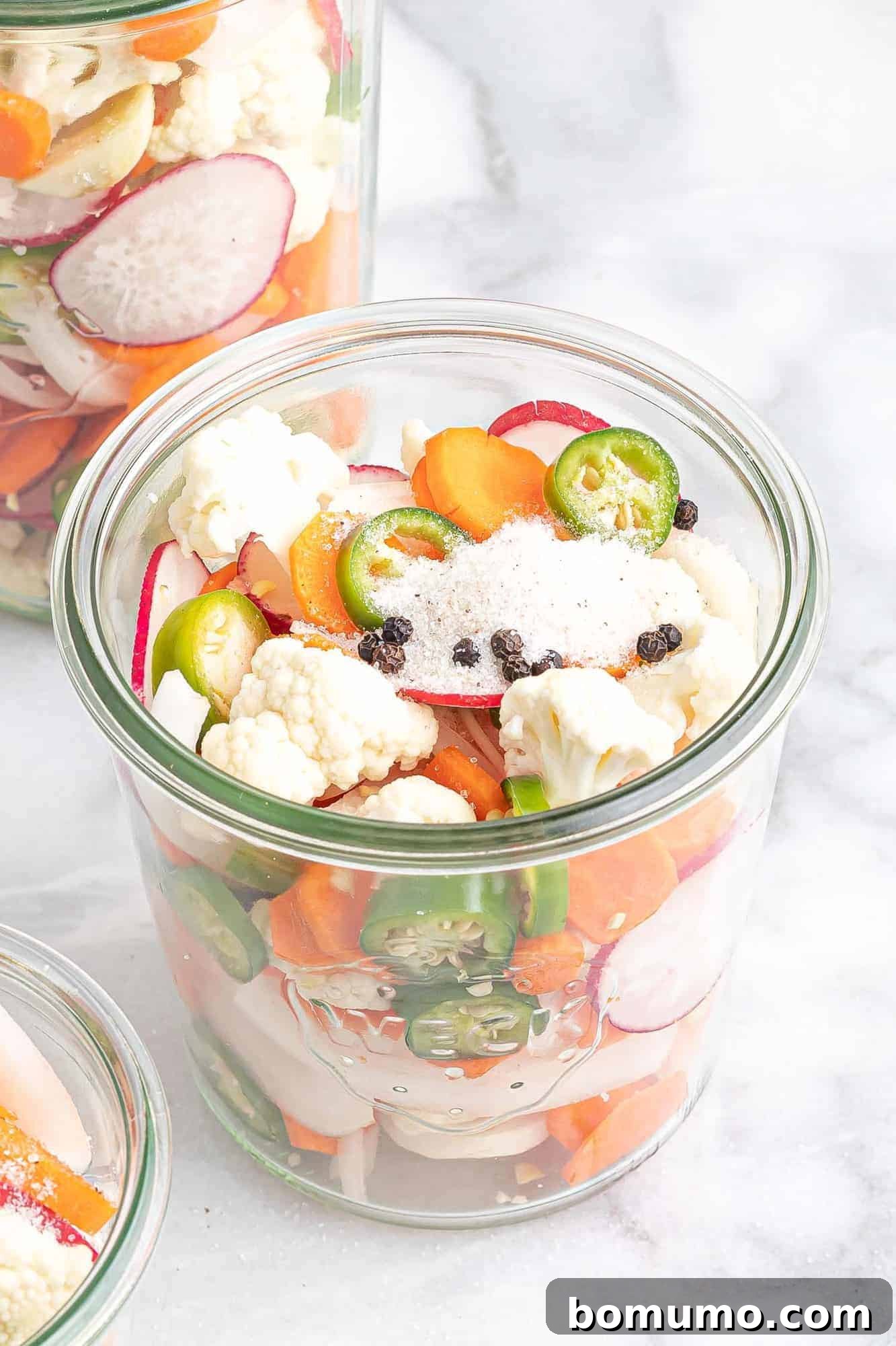 Cut vegetables in a glass jar, now topped with sugar, salt, and peppercorns, ready for the liquid brine.