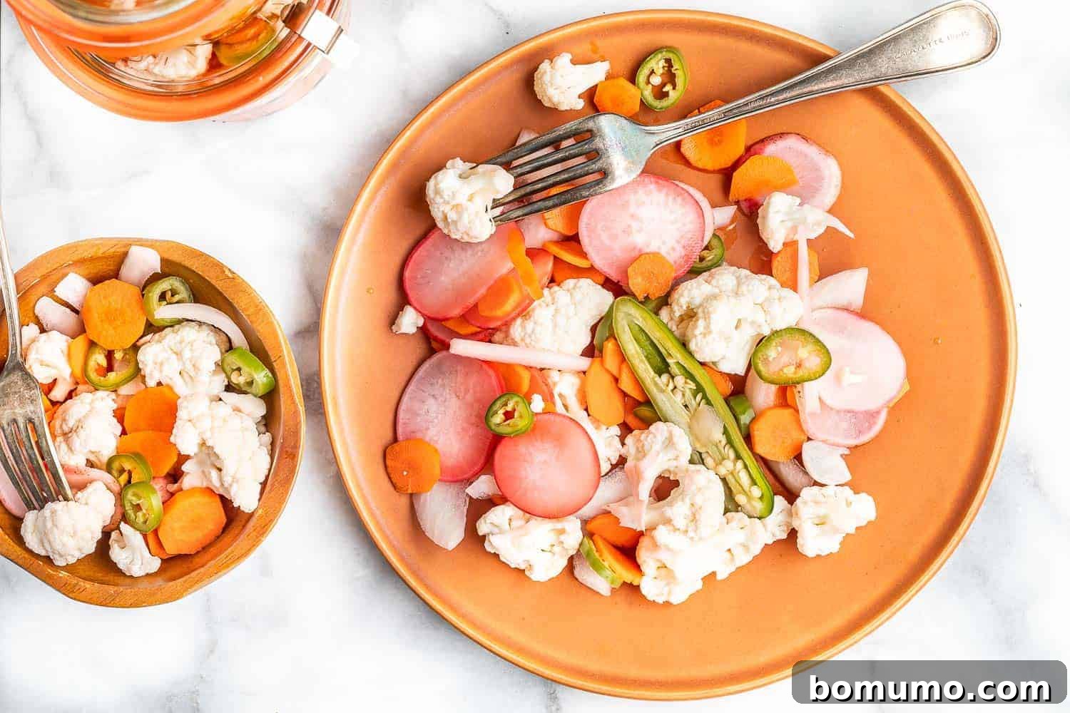 Mixed vegetables that have been pickled, served on an orange colored plate, garnished with fresh herbs.