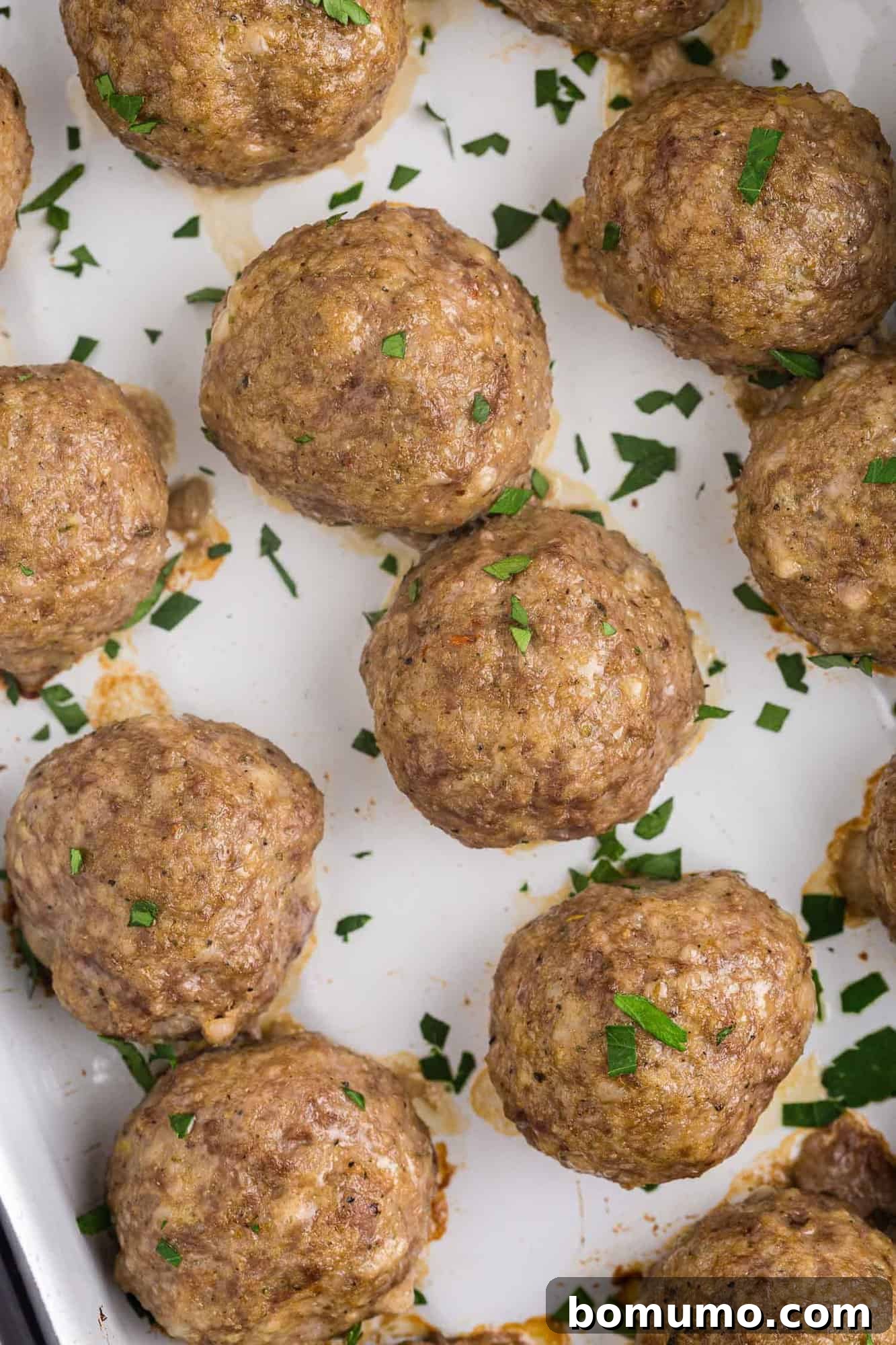 Overhead view of perfectly golden-brown baked meatballs without sauce, lightly garnished with fresh parsley.