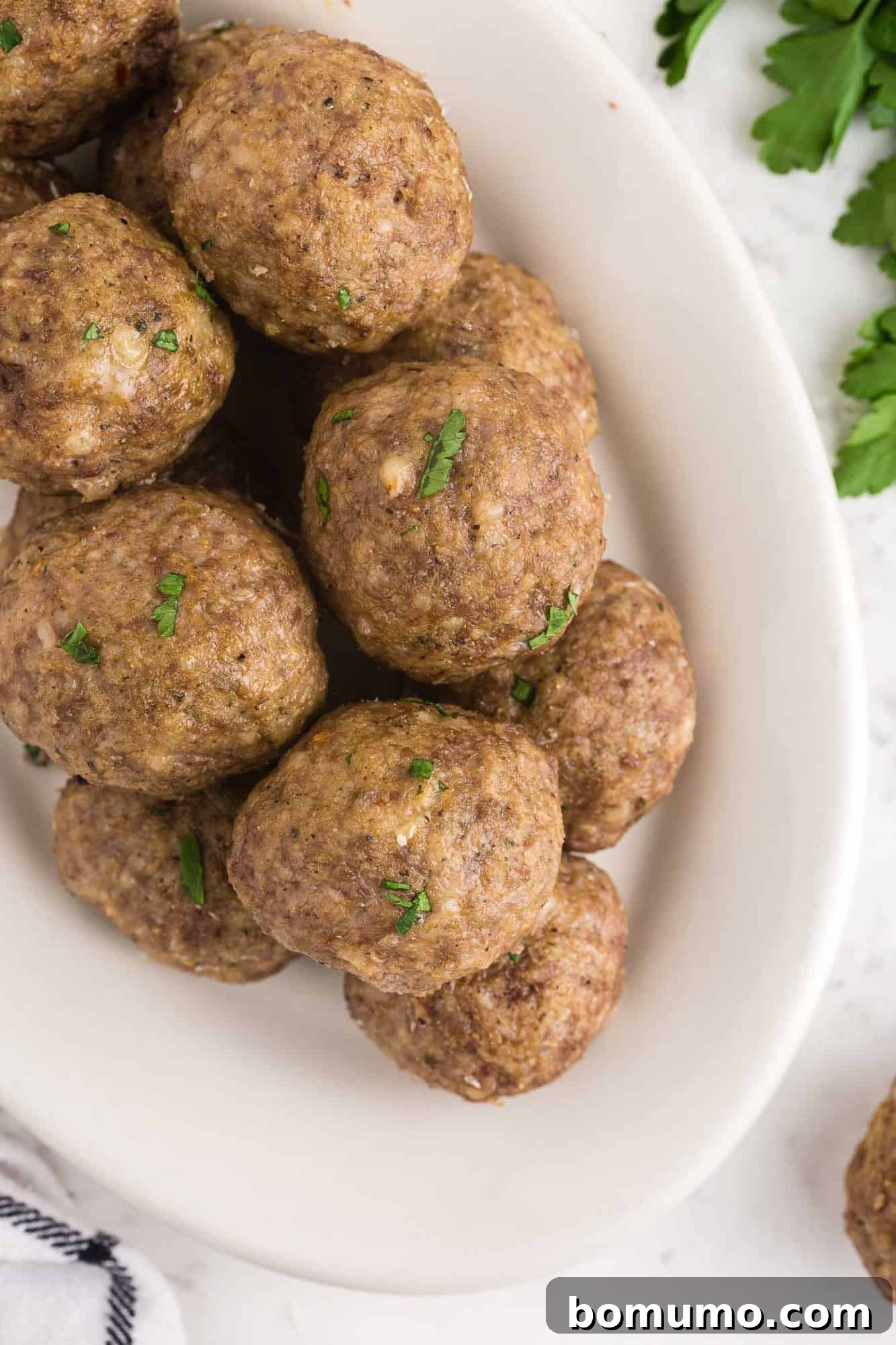 A platter generously piled with cooked meatballs, lightly sprinkled with fresh herbs, ready to be served.