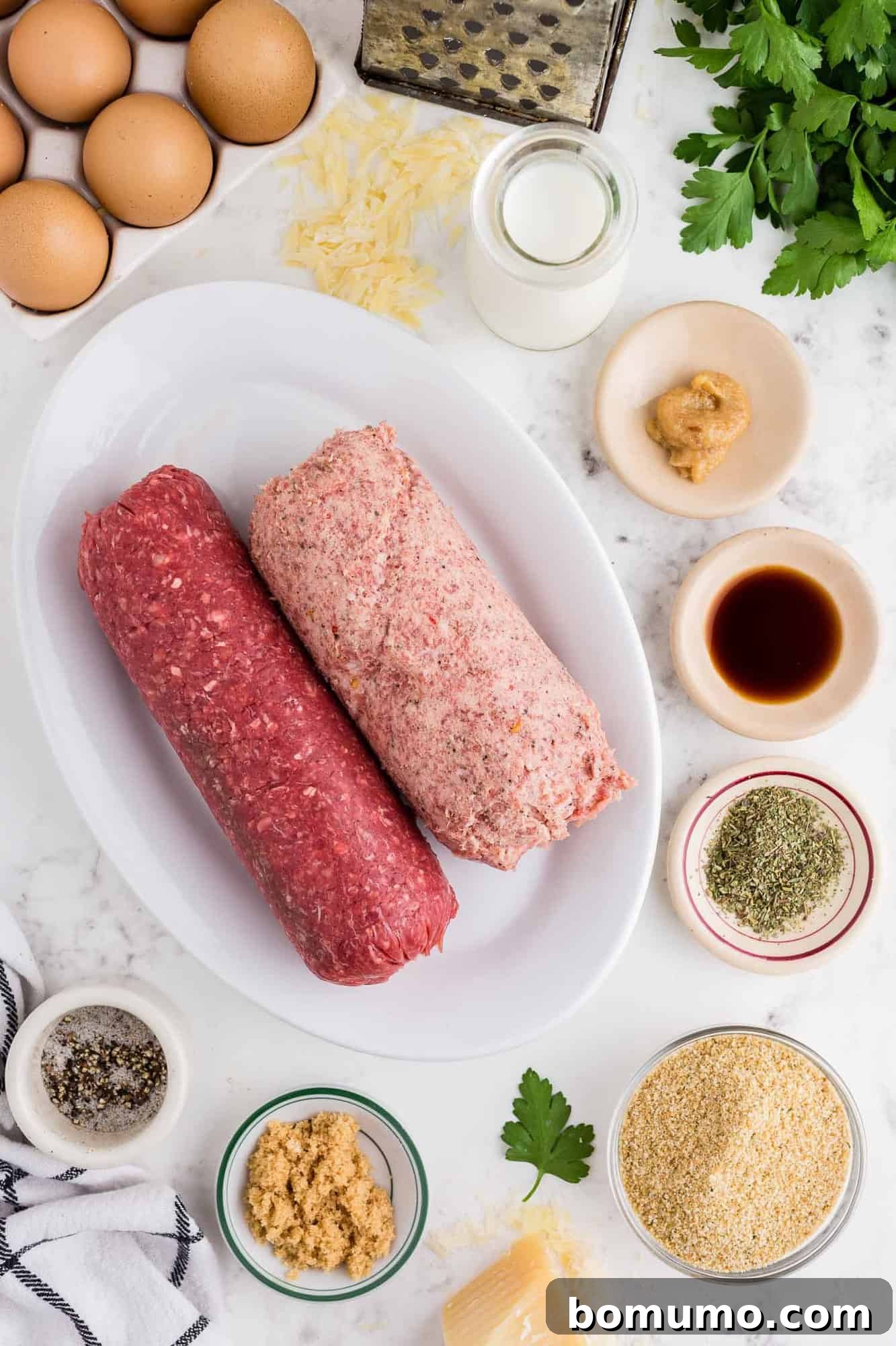 Overhead view of all the raw ingredients neatly laid out: ground meat, various spices, eggs, breadcrumbs, and cheese.