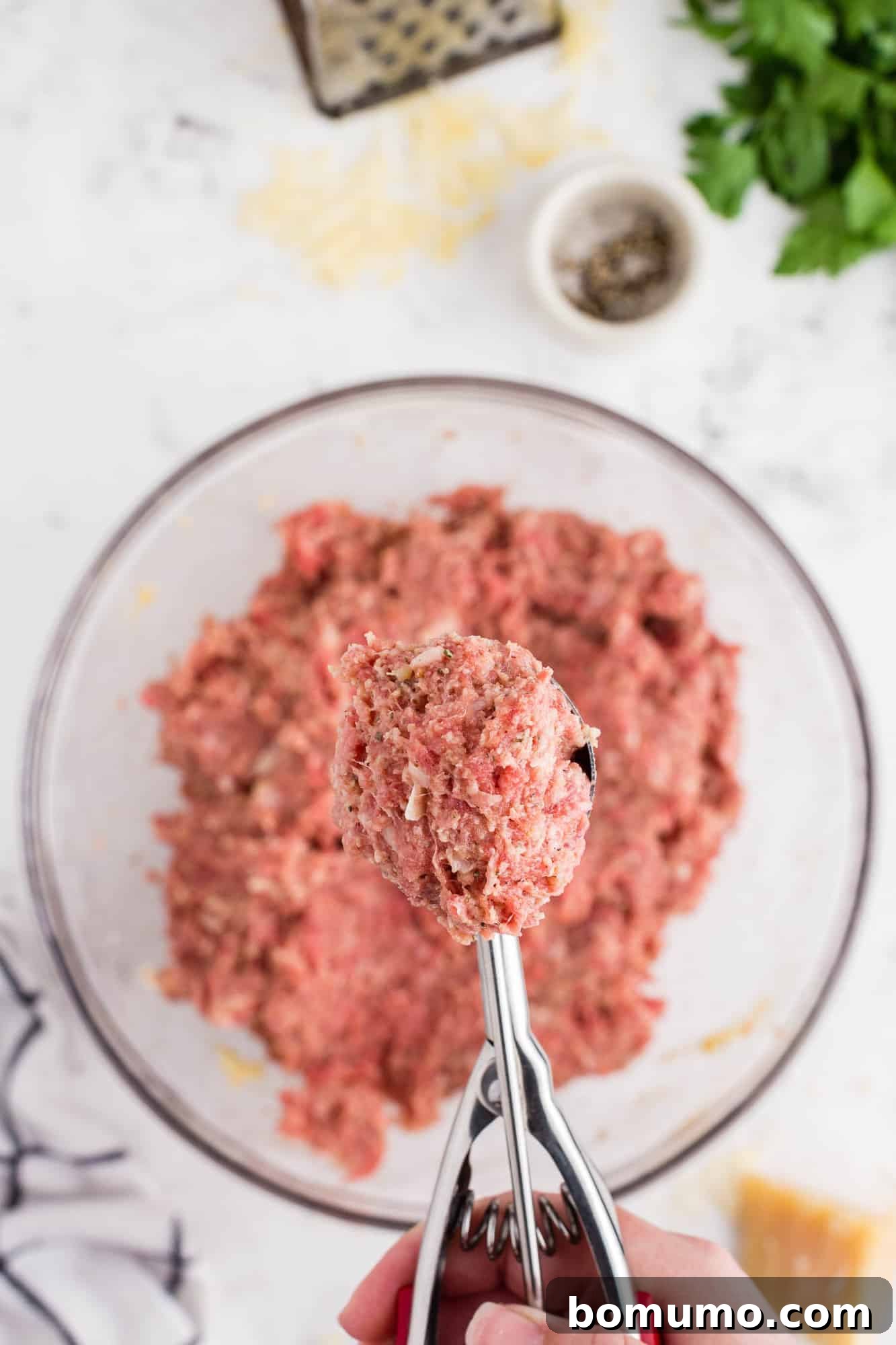 A scoop holding a portion of uncooked ground meat mixture, ready to be formed into a meatball.