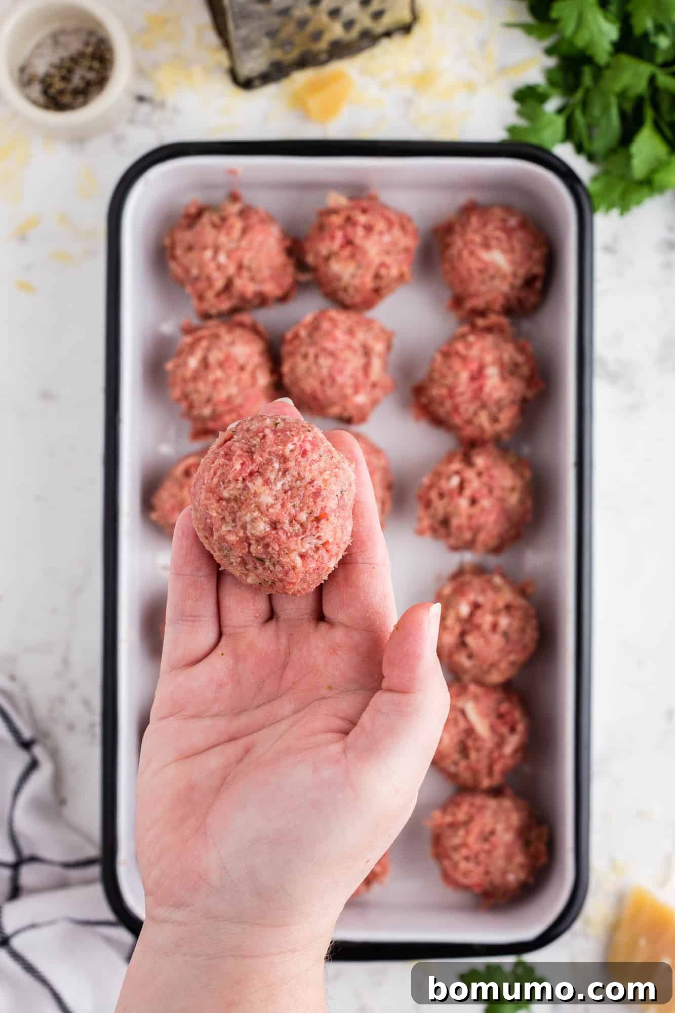 A hand gently shaping a perfectly round uncooked meatball.