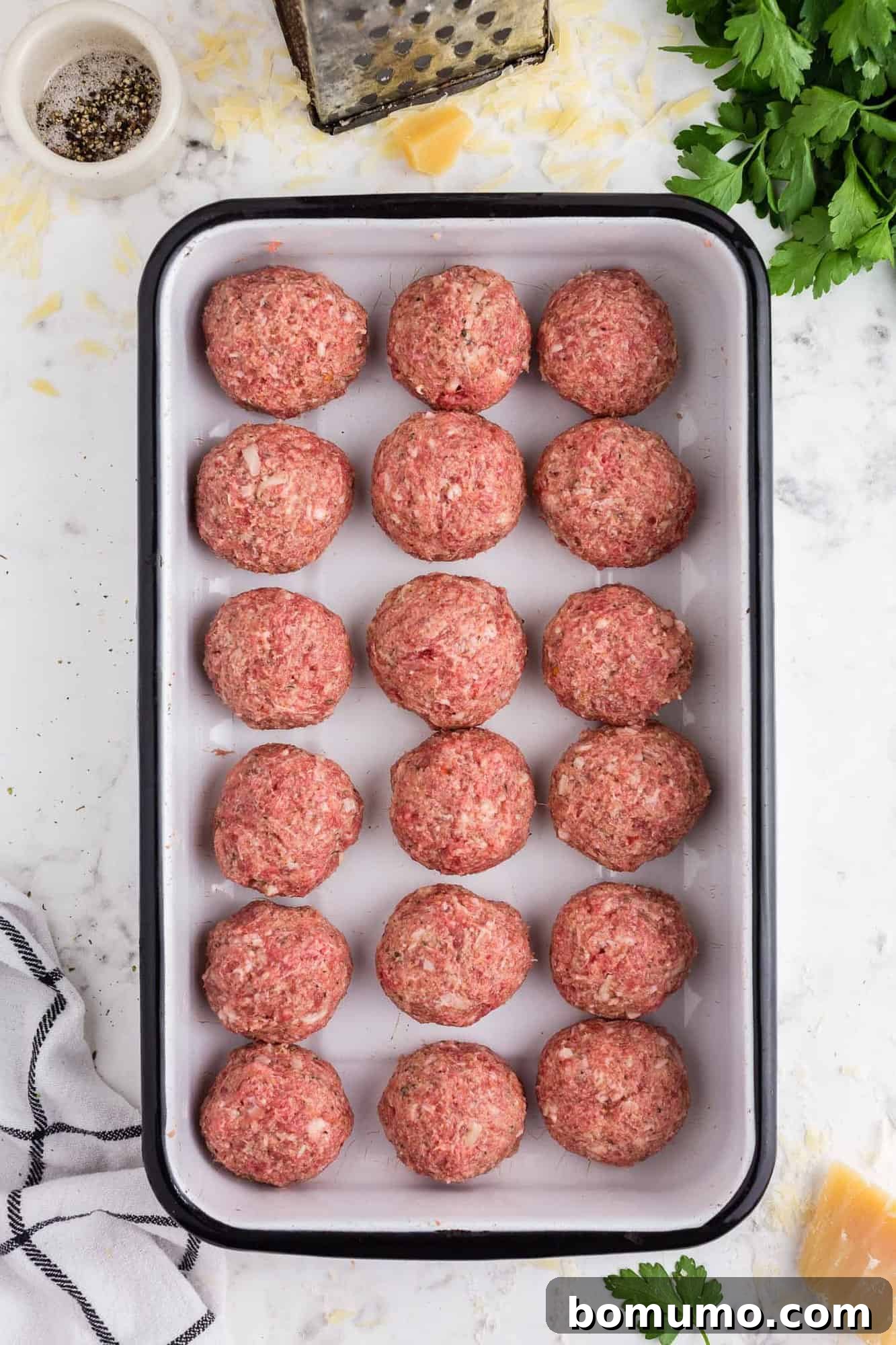 Overhead view of several uncooked meatballs neatly arranged in a baking pan, ready for the oven.