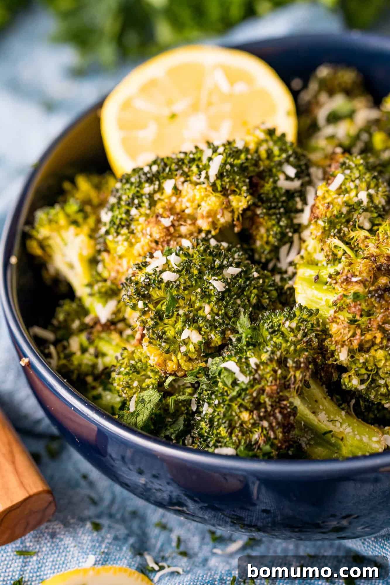 Crispy Lemon-Parmesan Roasted Broccoli 2 Crisp, golden-brown lemon roasted broccoli with grated Parmesan cheese and fresh lemon slices, presented in an elegant serving bowl.