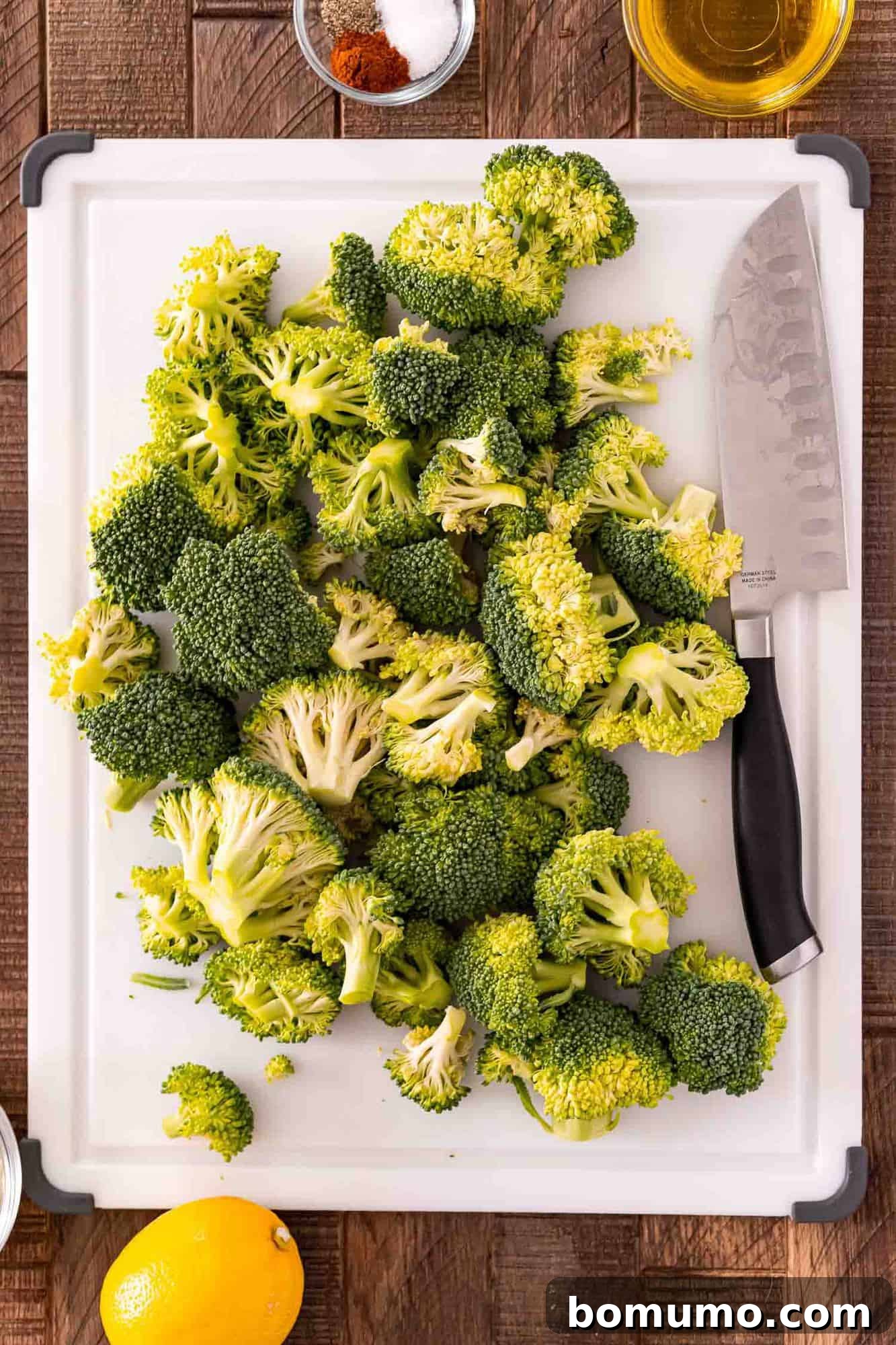 Crispy Lemon-Parmesan Roasted Broccoli 4 Broccoli florets neatly arranged on a white cutting board, accompanied by a chef's knife, ready for preparation.
